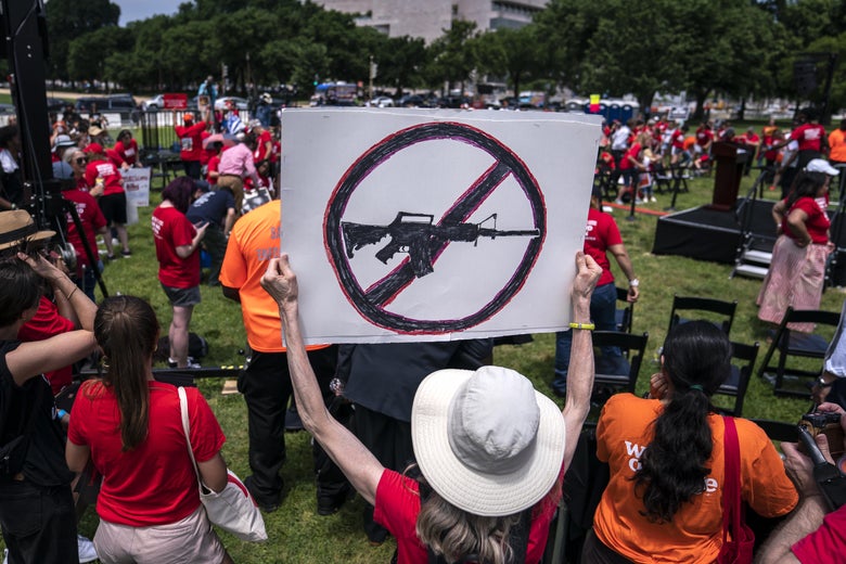 A protester in an red shirt holds up a sign with a circle with a slash through it over the silhouette of an AR-15.
