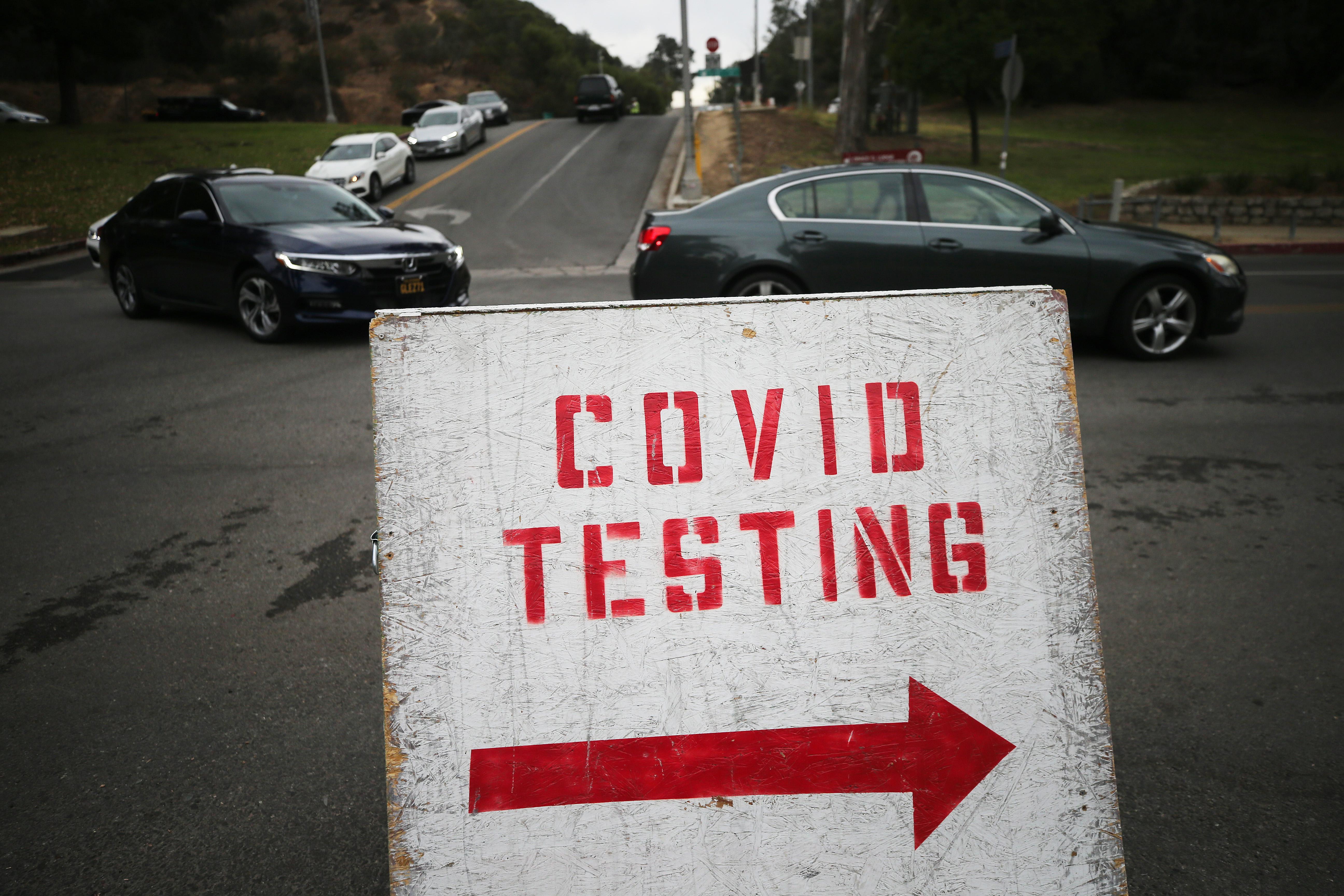 Cars lined up to enter the COVID-19 testing site at Dodger Stadium in Los Angeles, with a sign marked "COVID TESTING" in the foreground