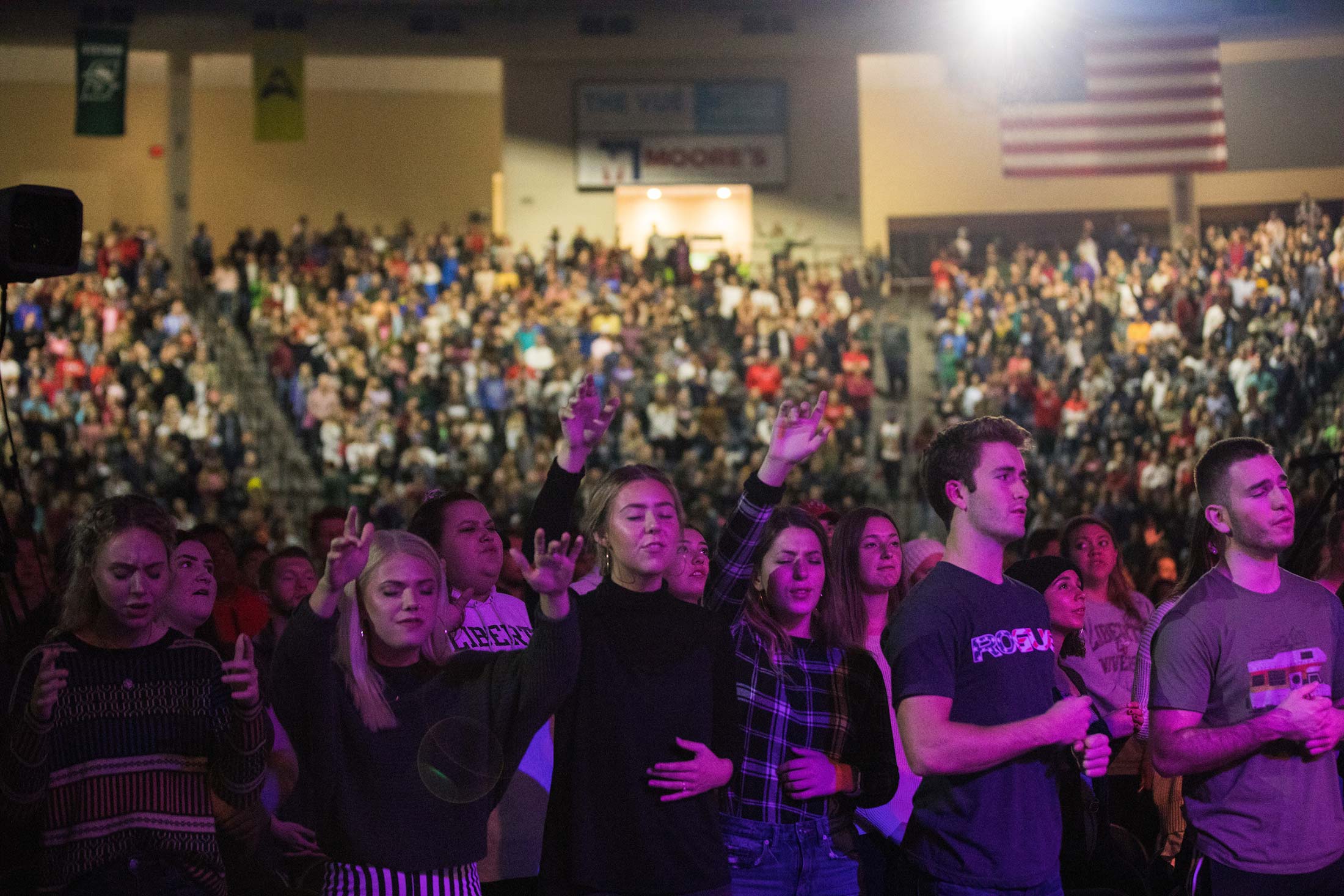 Liberty University students inside the arena. Some raise their arms and close their eyes in worship.