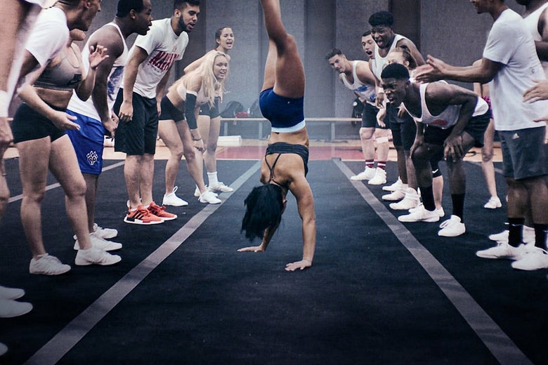 A cheerleader doing a flip while her teammates cheer her on.