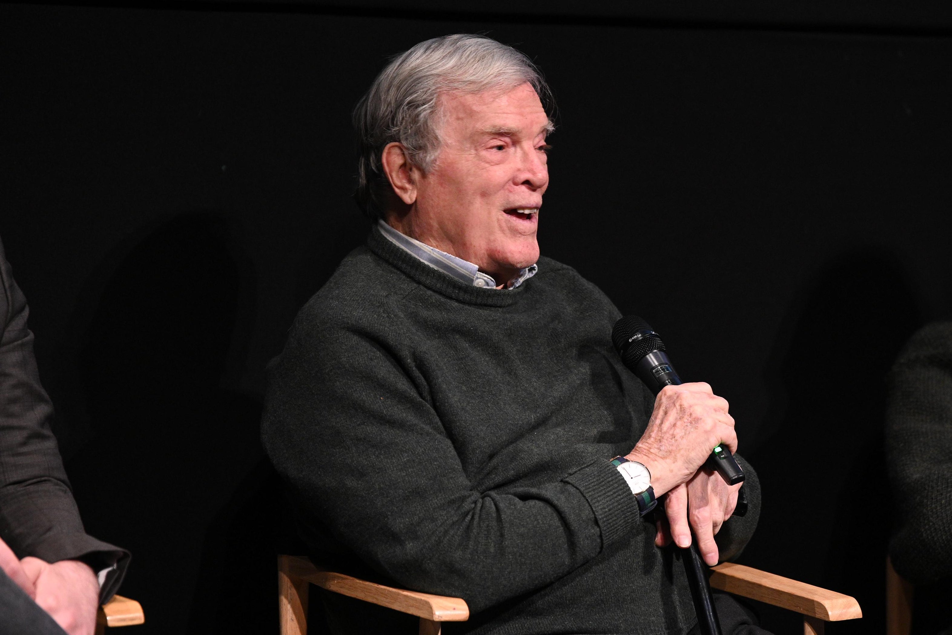 D.A. Pennebaker, sitting in a director's chair onstage, laughs during a Q&A.