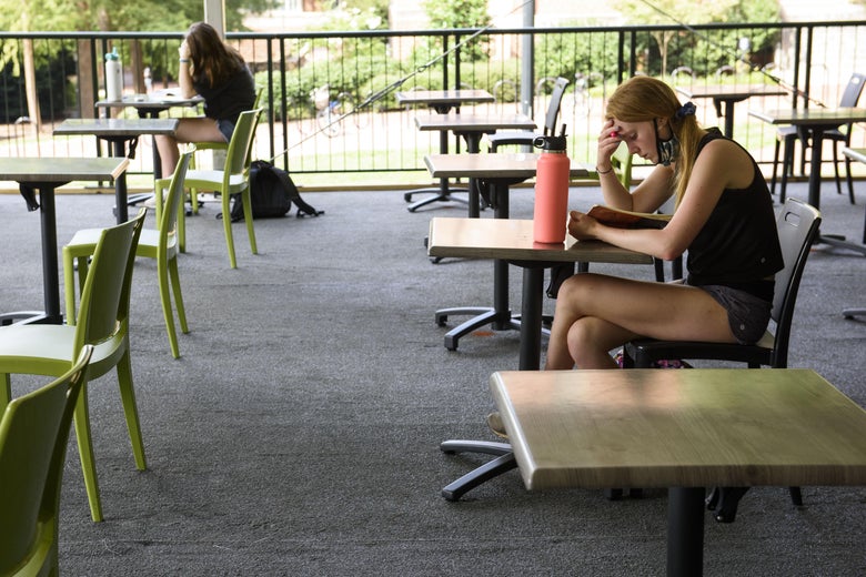 Two young people sit at tables far apart from each other