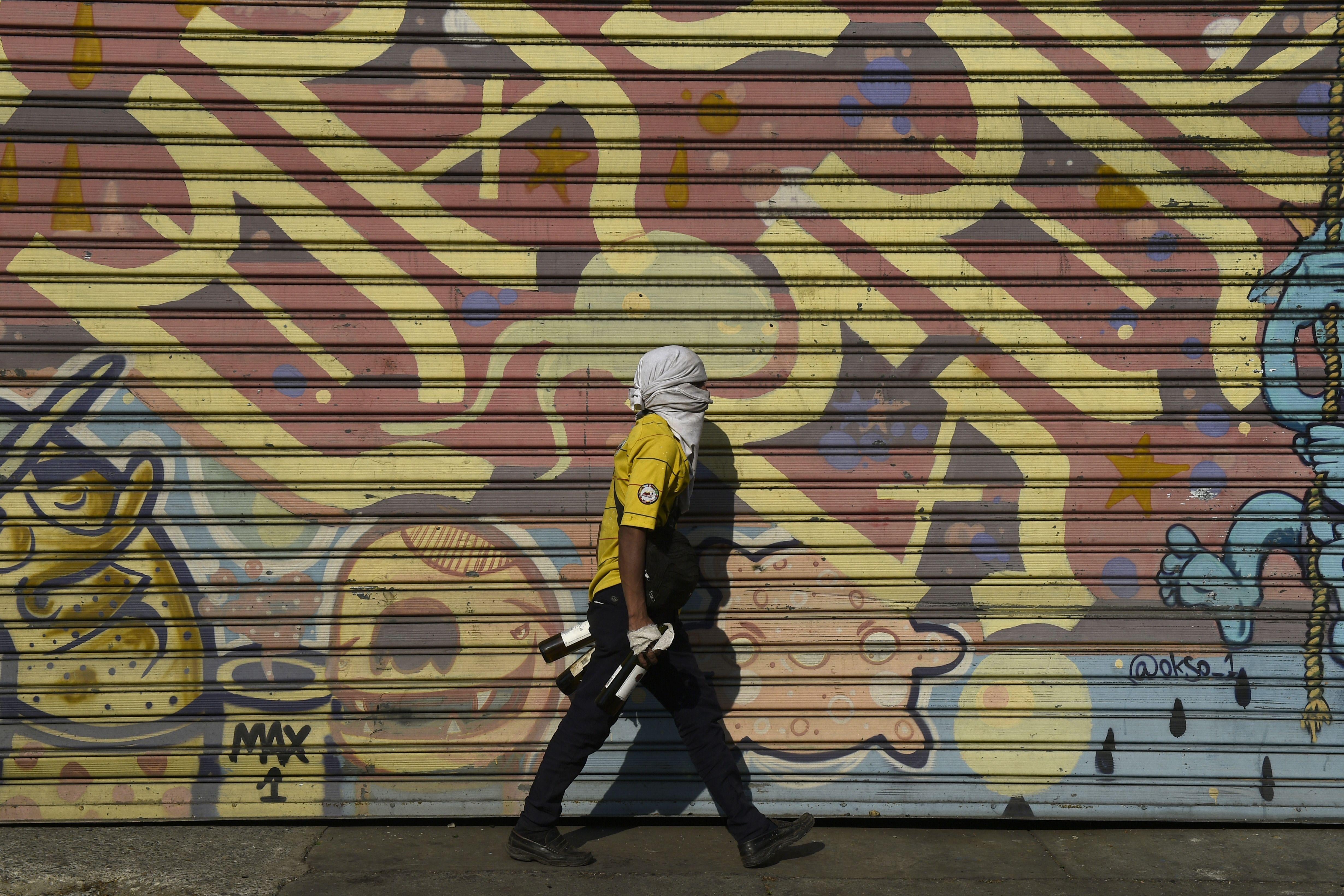 An opposition demonstrator walks by a graffiti.