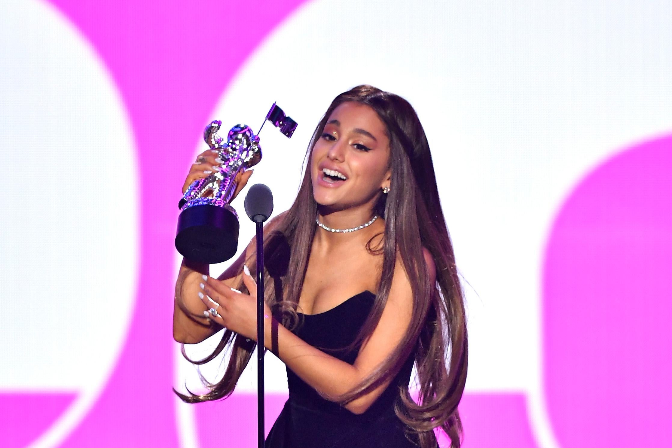 Ariana Grande holds a statuette up as she speaks into a microphone.