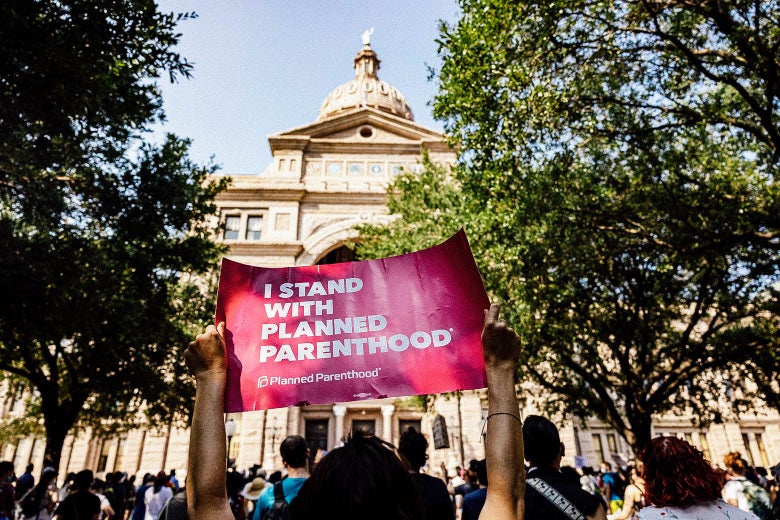 A protester standing in a crowd in front of the Capitol holds up a sign that says "I Stand With Planned Parenthood"