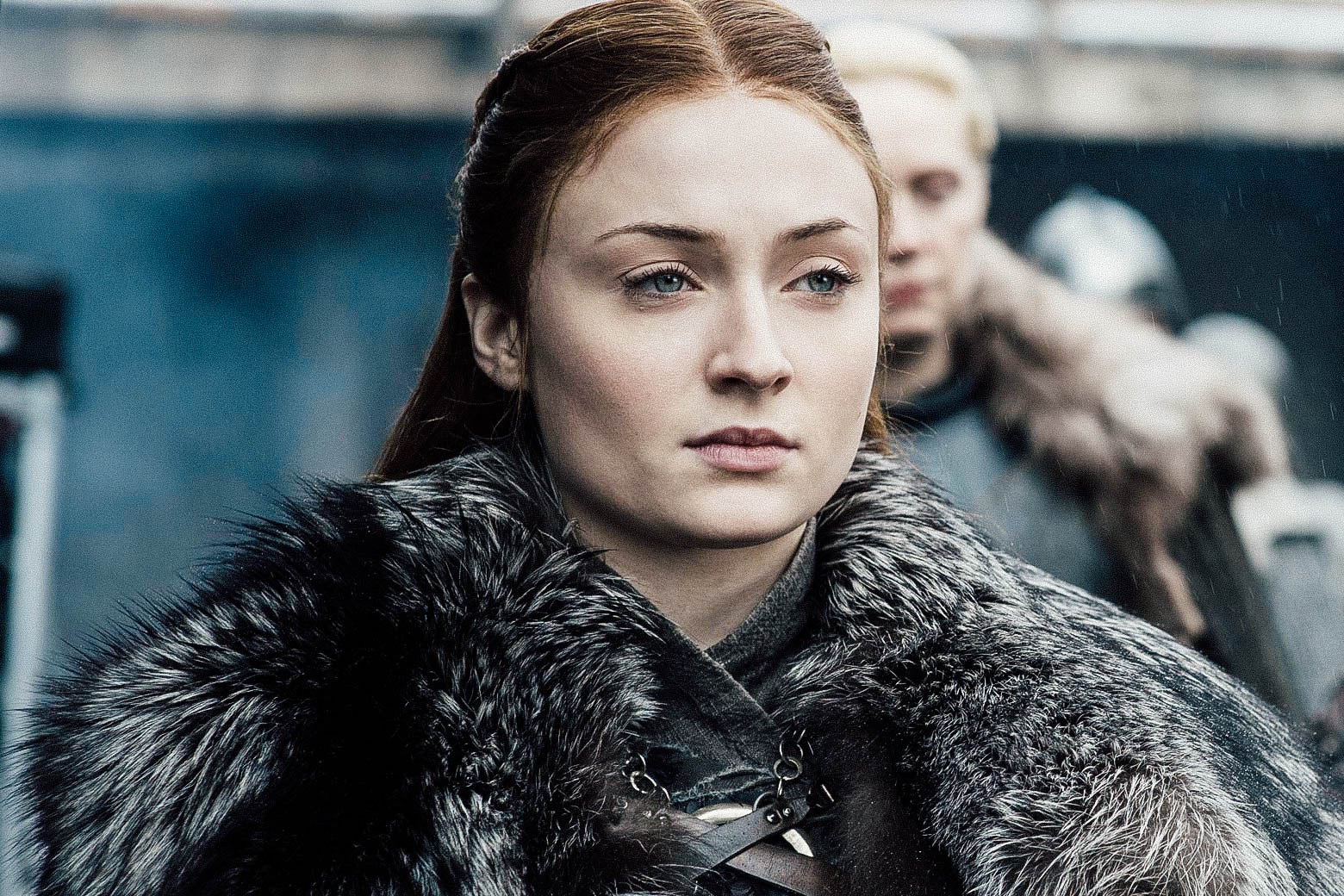 Sophie Turner as Sansa Stark stands while wearing a fur coat in this still from Game of Thrones.