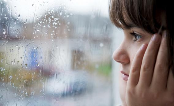 Young child looking out of window on rainy day.