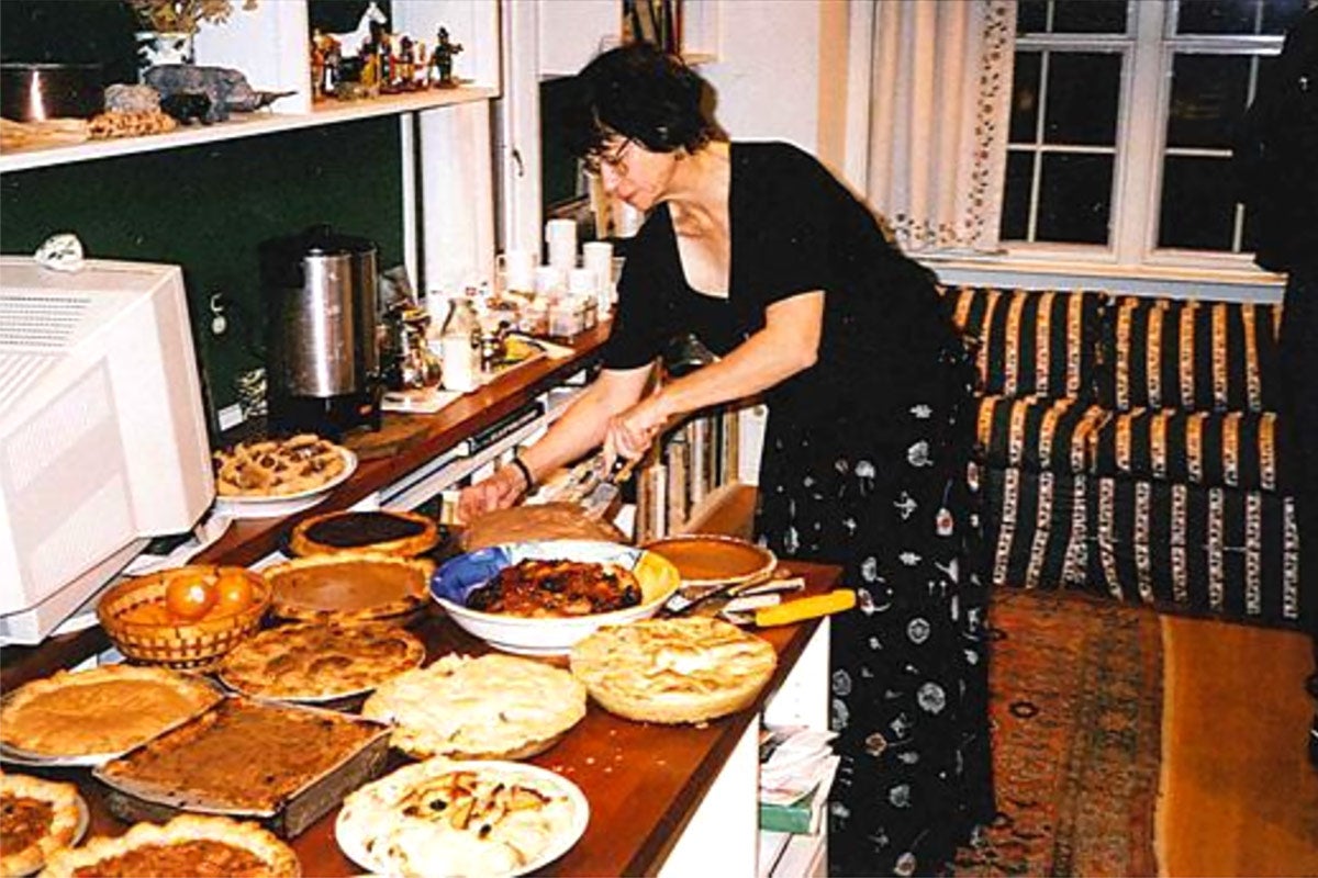 A woman in a dark dress and glasses standing over a plethora of Thanksgiving pies.
