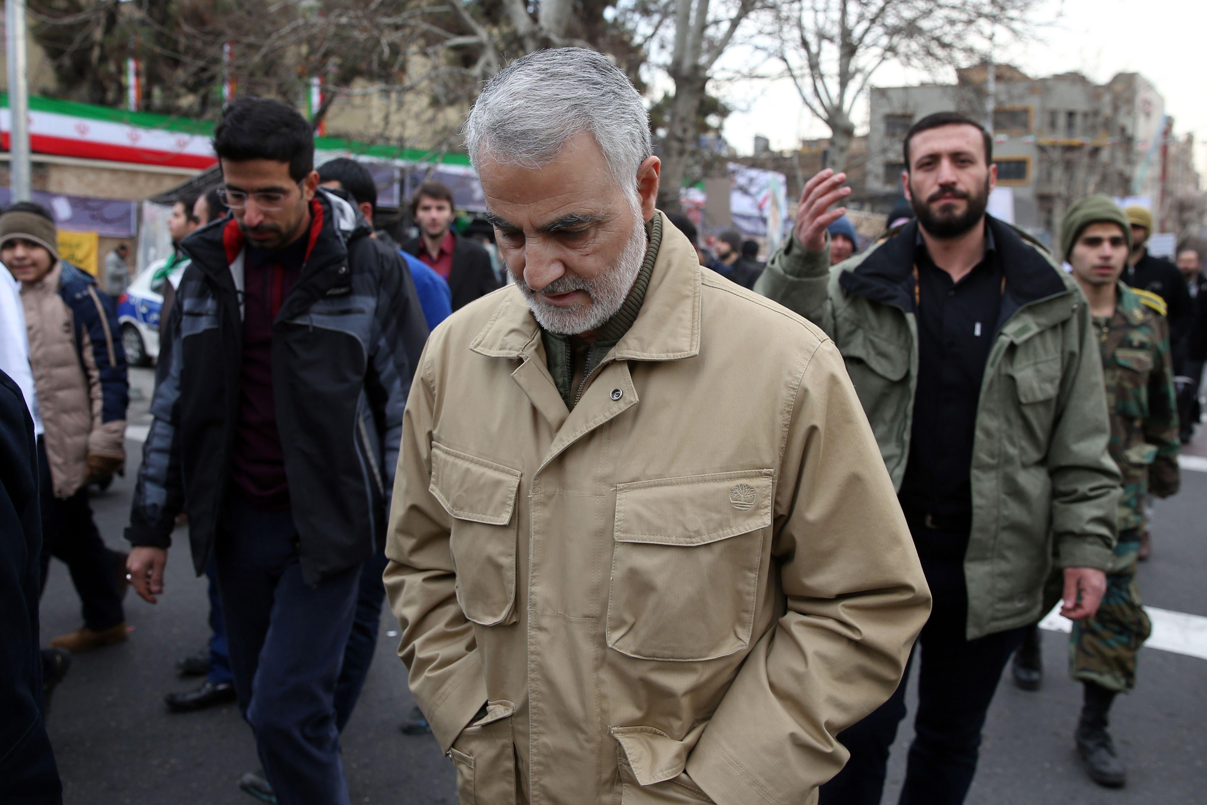 Qassem Soleimani, wearing civilian clothes, walks during a street procession with his eyes down.