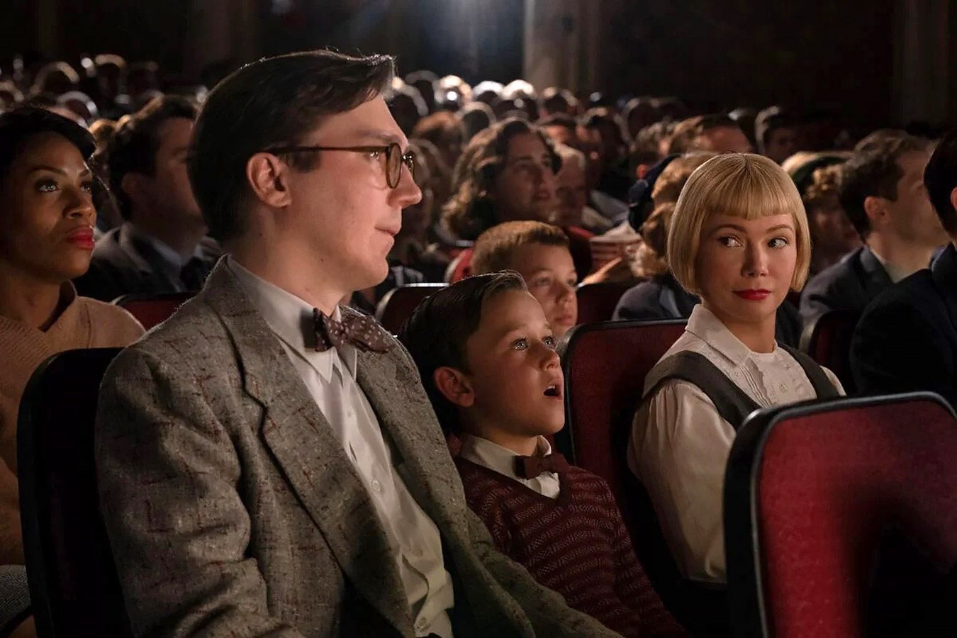 A family of three in 1950s garb watch a movie in a movie theater.
