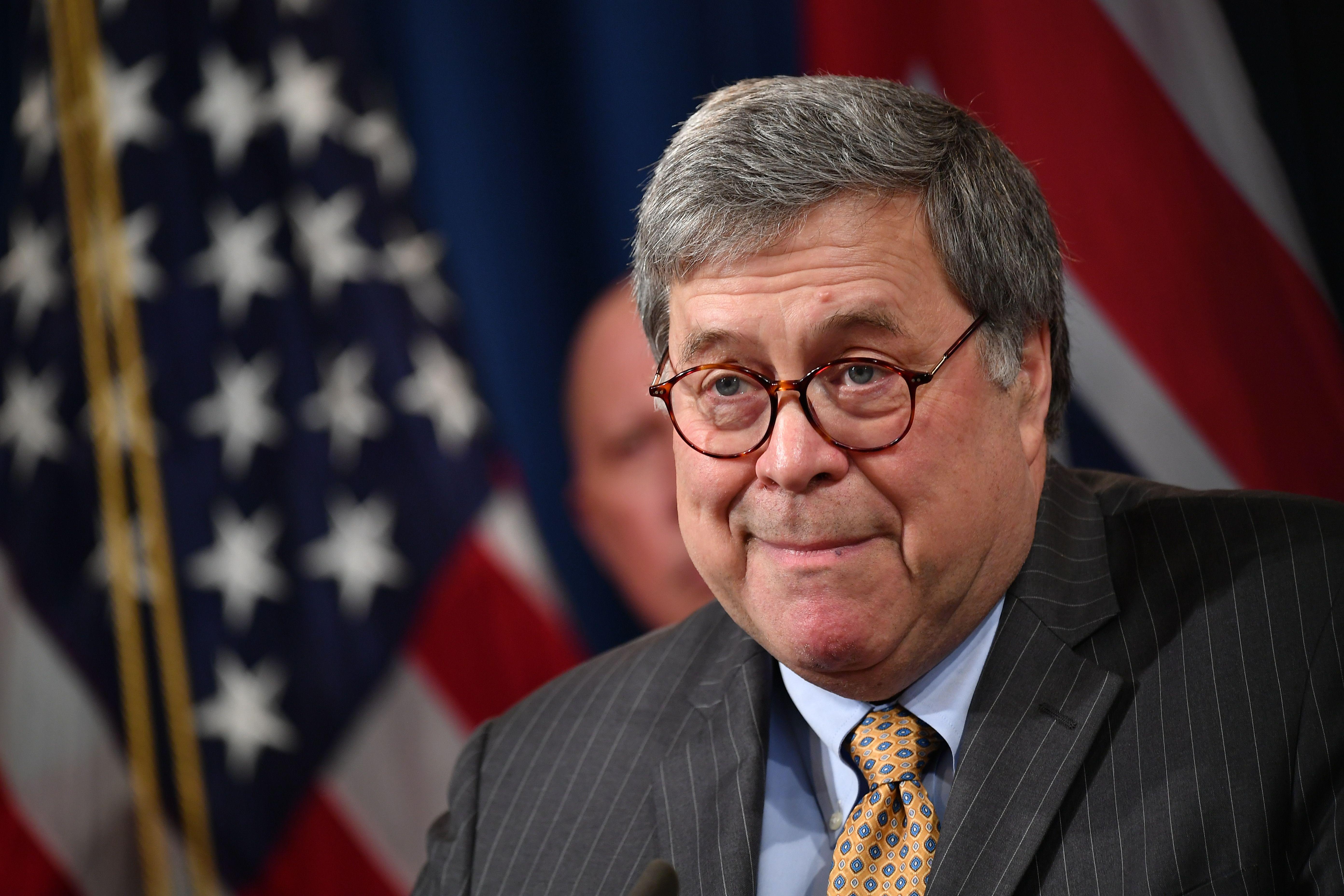 Barr smiles widely in front of the American flag.