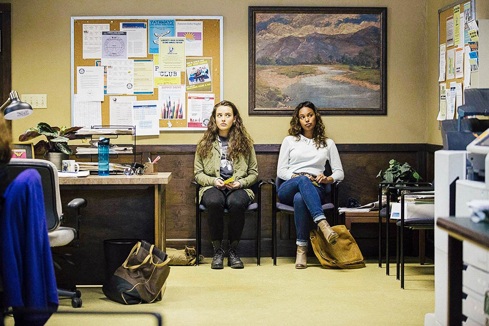 Alisha Boe and Katherine Langford sit in chairs against a wall in 13 Reasons Why
