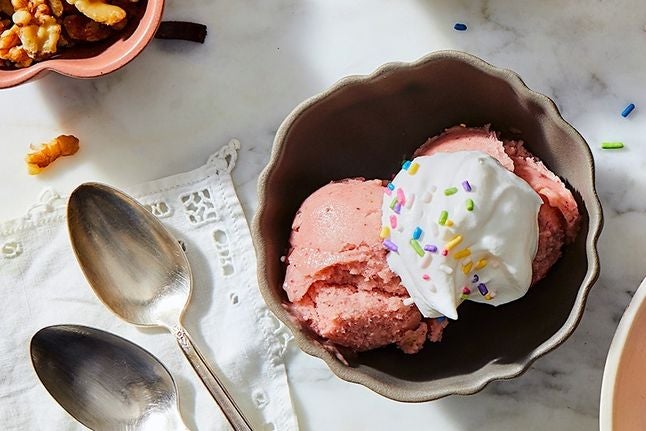Bright pink ice cream topped with whipped cream and rainbow sprinkles.