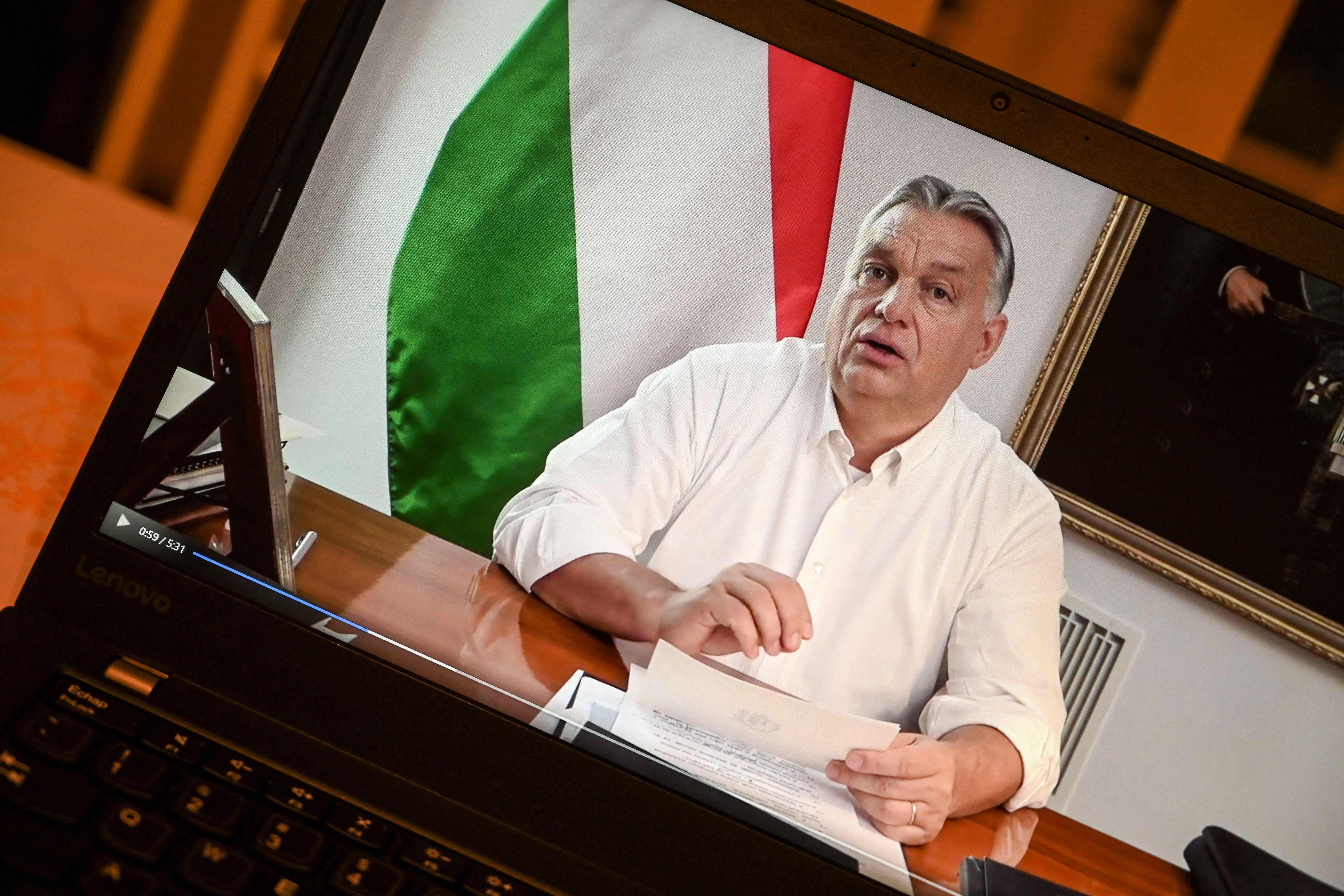 A laptop screen shows a man sitting at a desk, the Hungarian flag behind him.