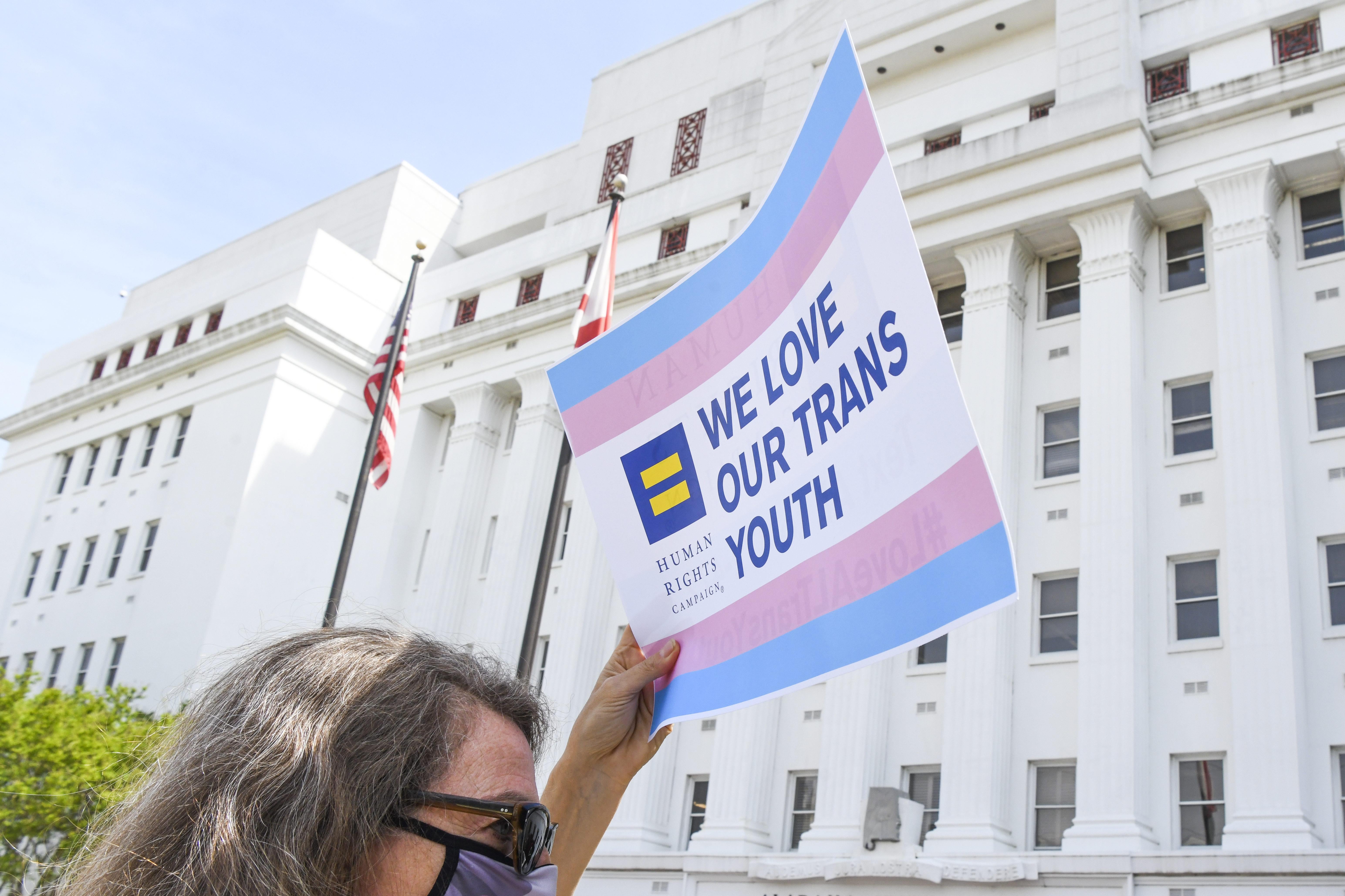 A woman holds a sign that reads "We love our trans youth" outside the Alabama state house.