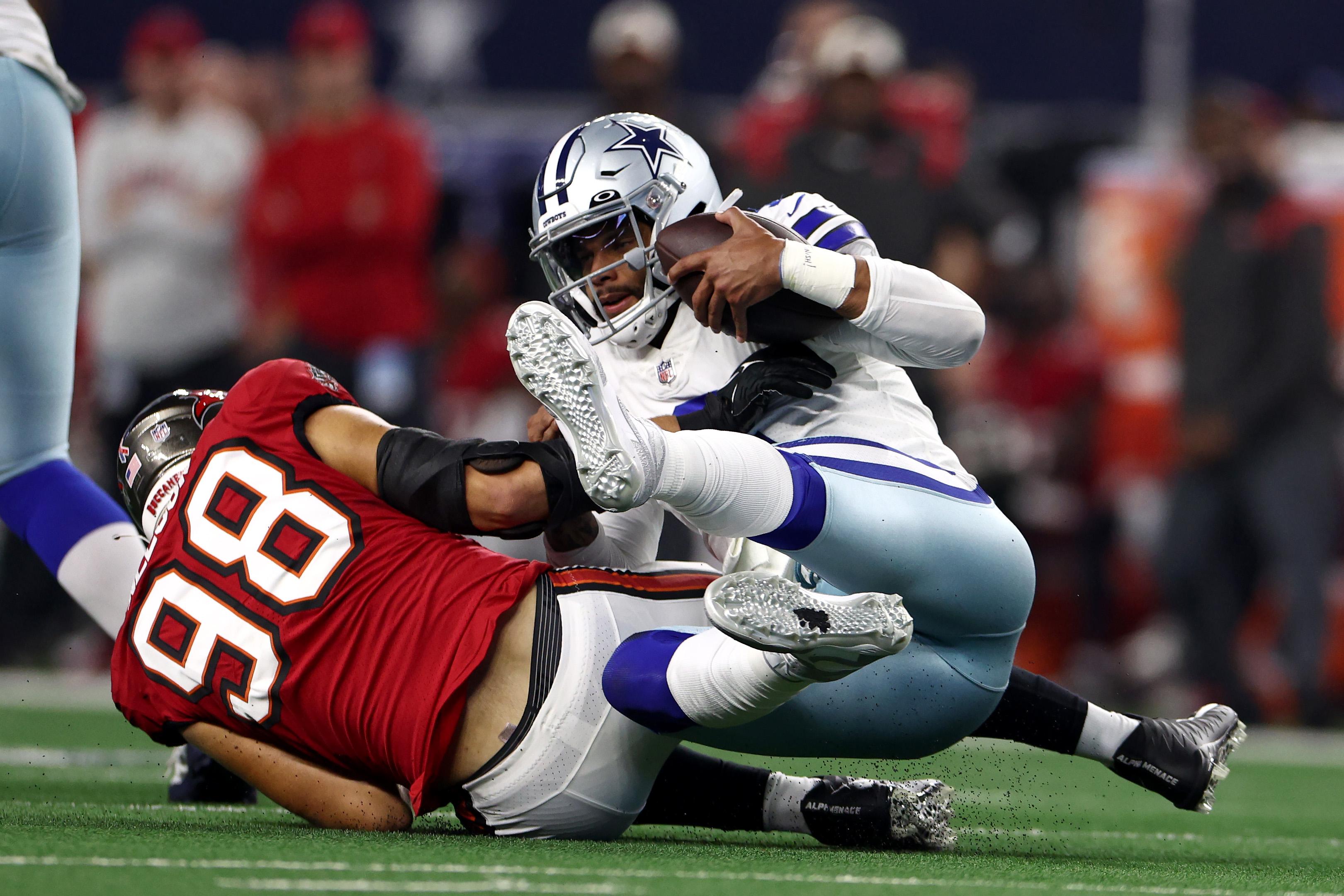 Dak grips the football and grimaces as he gets pulled to the ground by a giant Buccaneer
