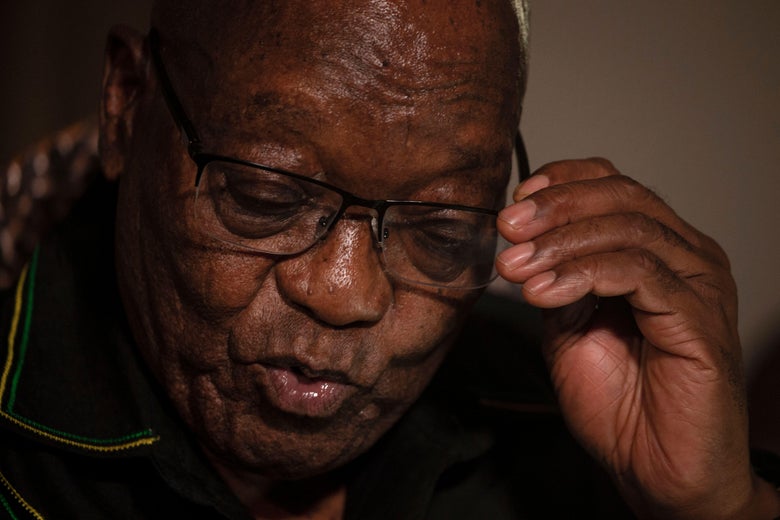A close up of Zuma lifting his hand to take off his glasses.