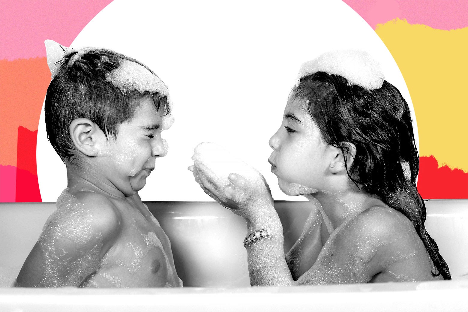 Two children sit in a bathtub, and one blows bubbles at the other.