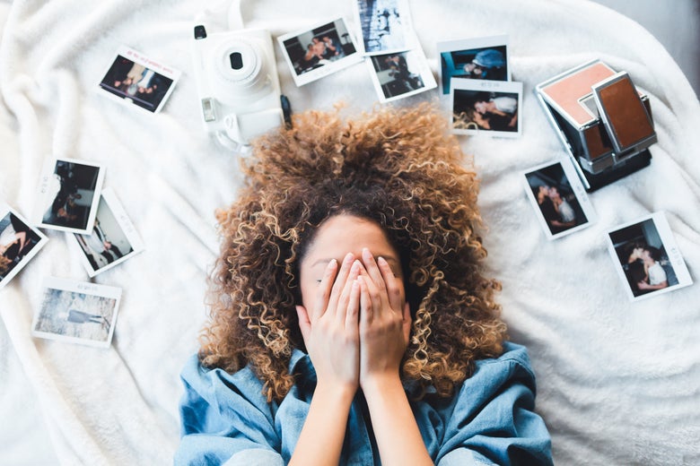 A woman on a bed surrounded by photos, with her hands on her face.