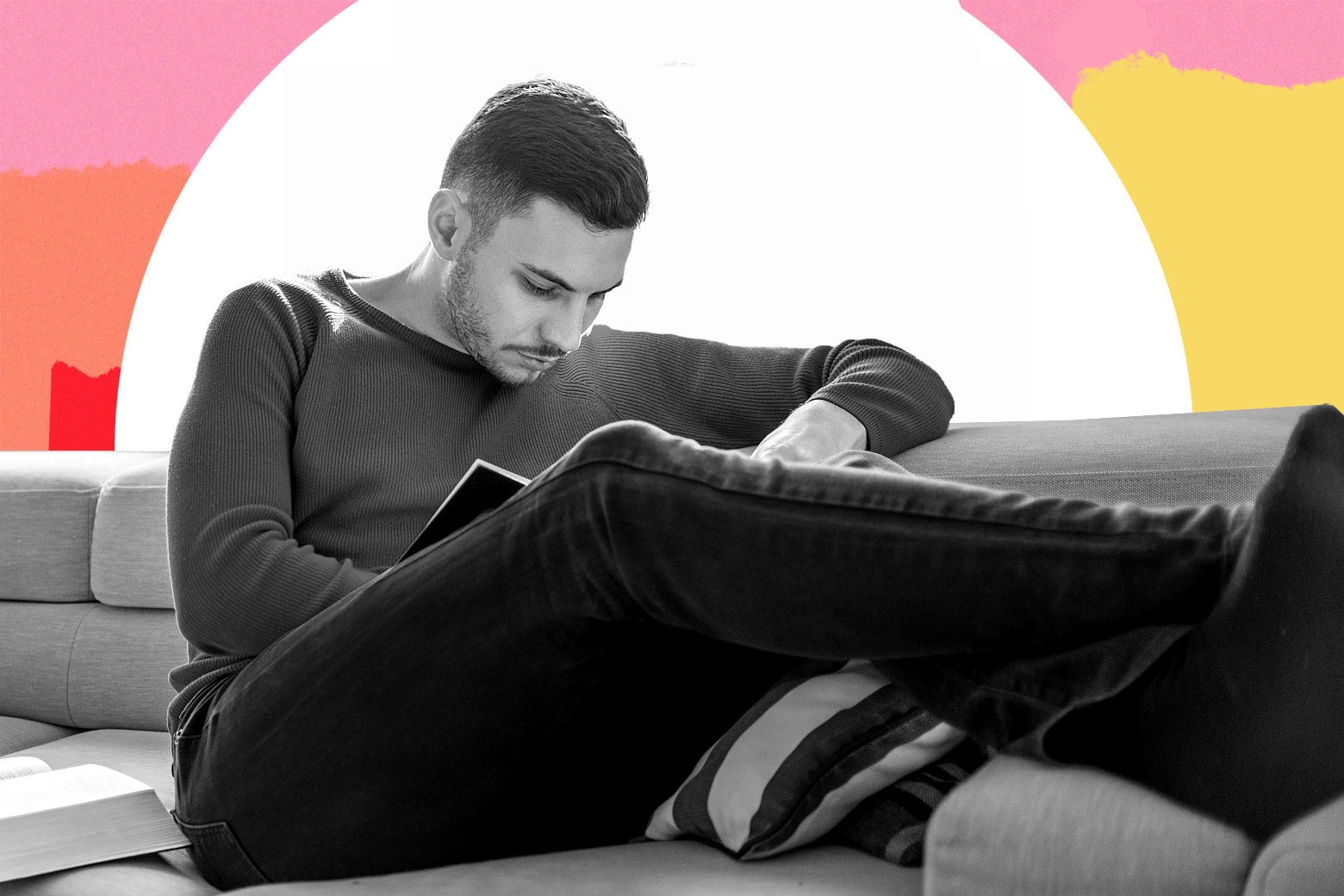 A young college student man reads a book on a couch.