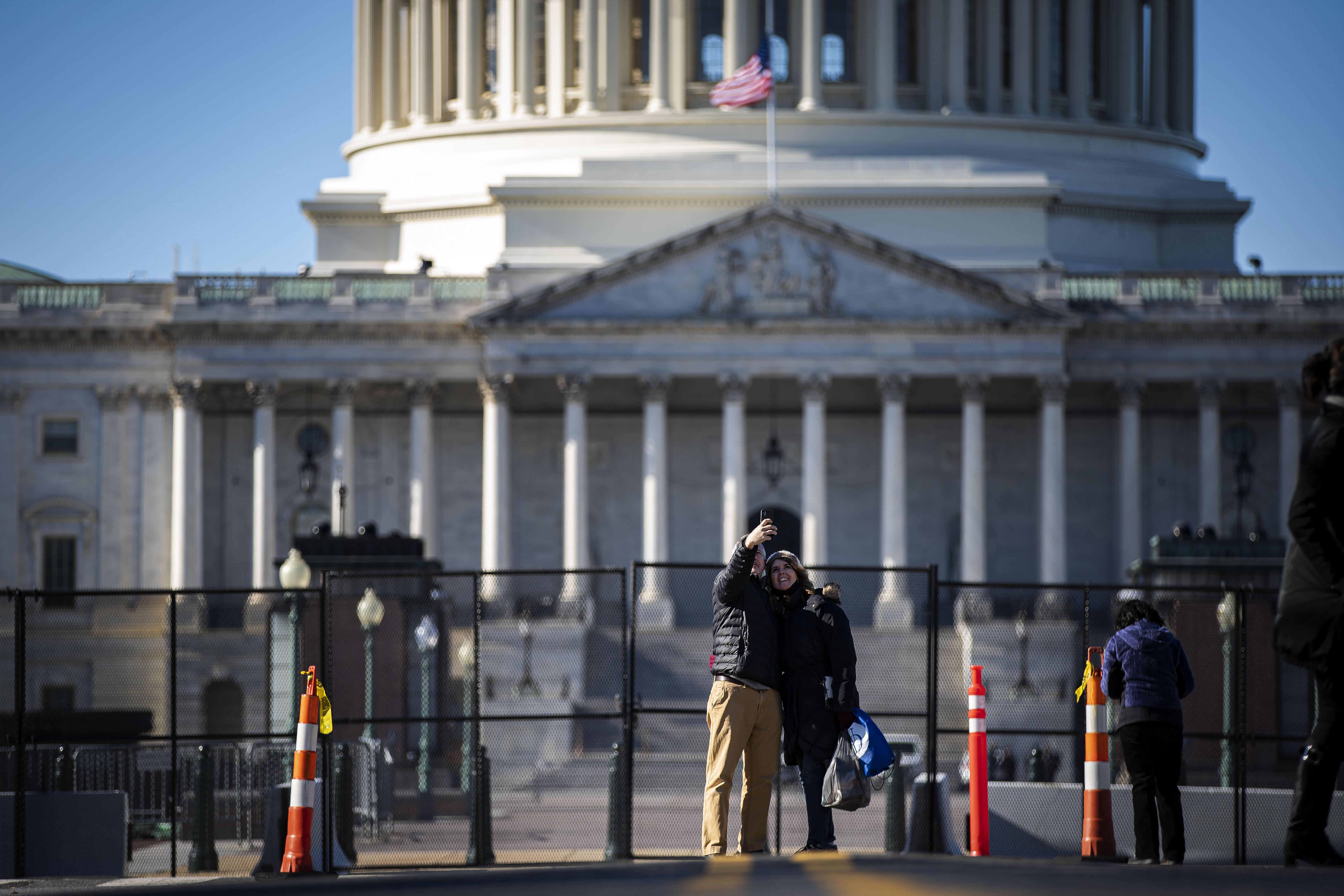 A smiling couple takes a selfie in front of the new security fence outside the Capitol dome