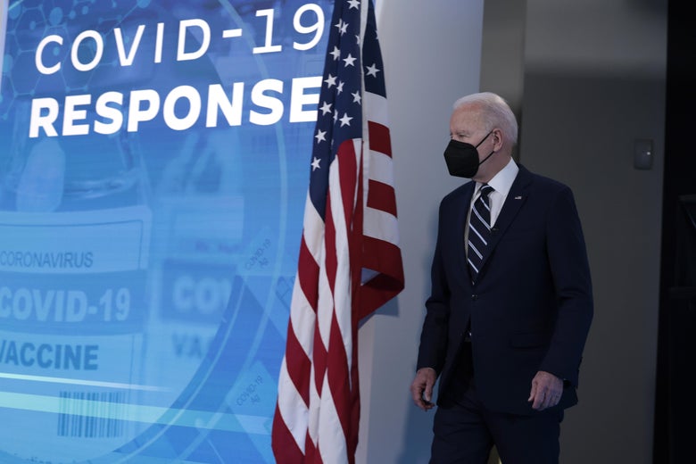 Joe Biden in a mask walking onstage beside an American flag and a screen that says "COVID-19 Response"