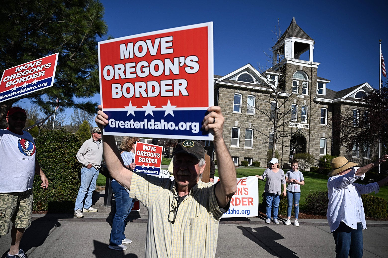 Multiple protestors stand outside a gray government building holding signs that say "Move Oregon's Border: GreaterIdaho.org."