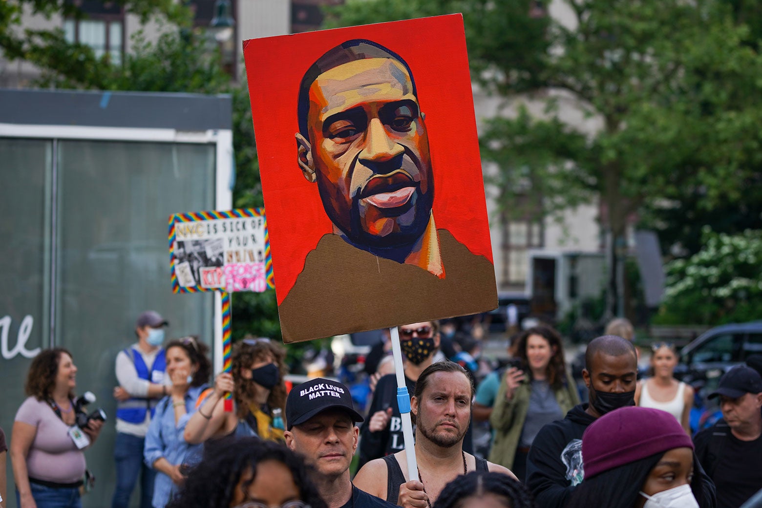 People at a gathering have signs held high with an illustration of George Floyd's face on them.