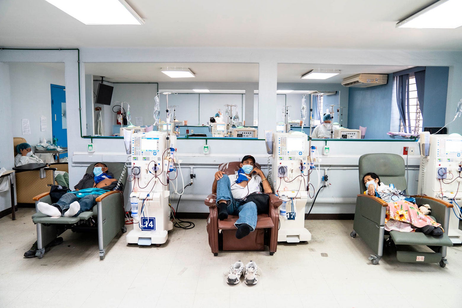 Three male patients recline in hospital chairs, hooked up to dialysis machines.