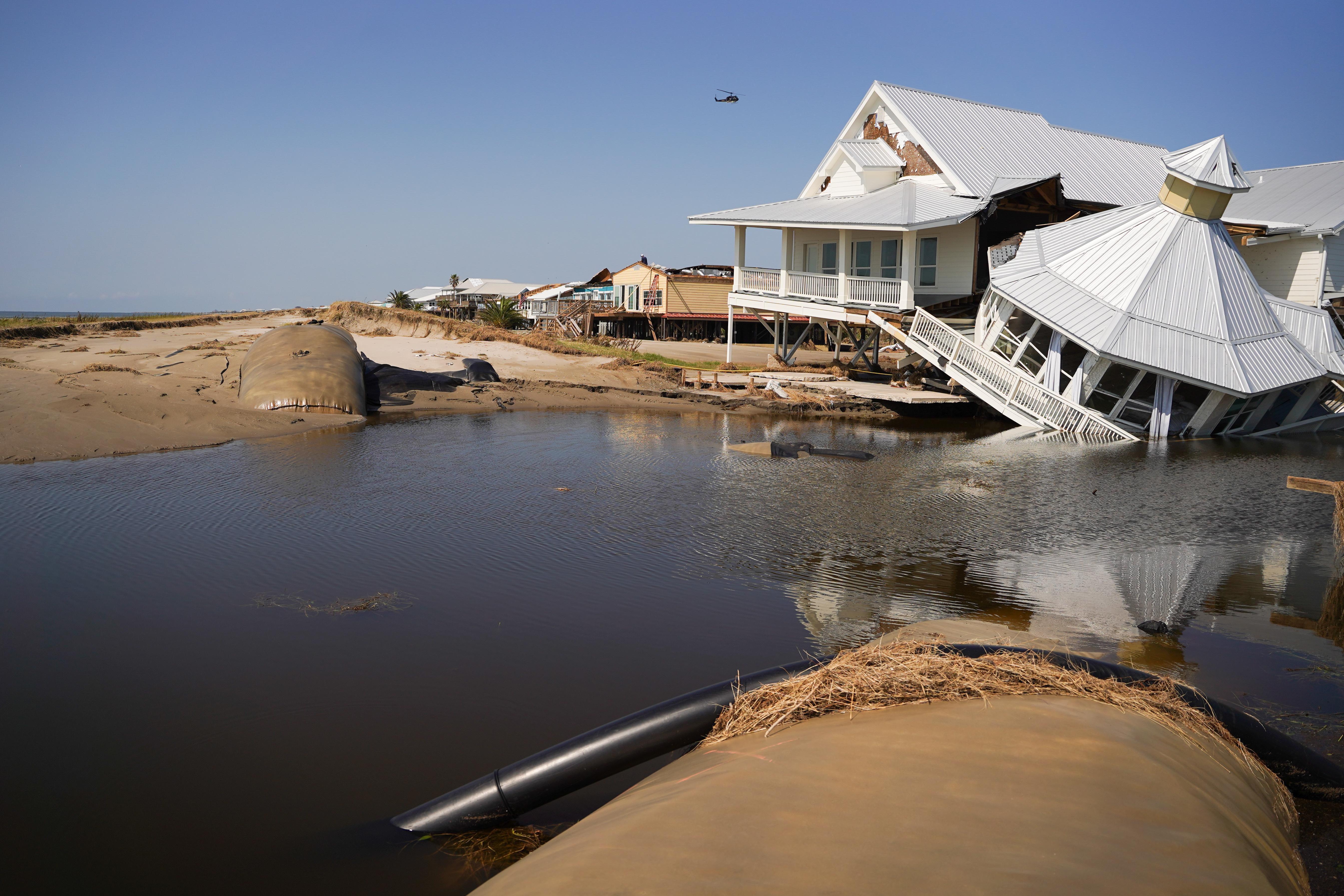 A beachfront house on stilts on a clear day. Half of it has sunk into the rising water.