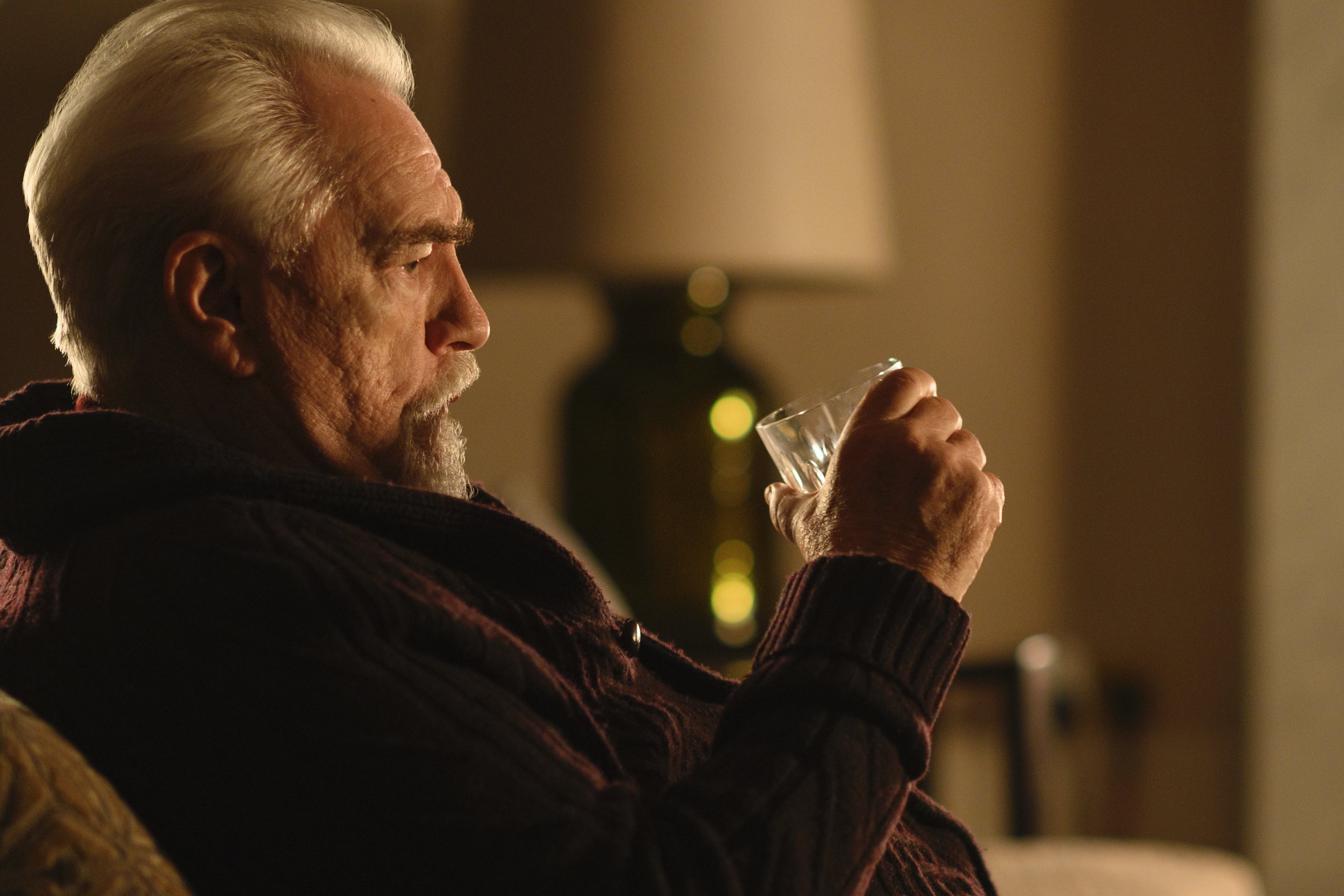Brian Cox pouts on a couch holding a glass.