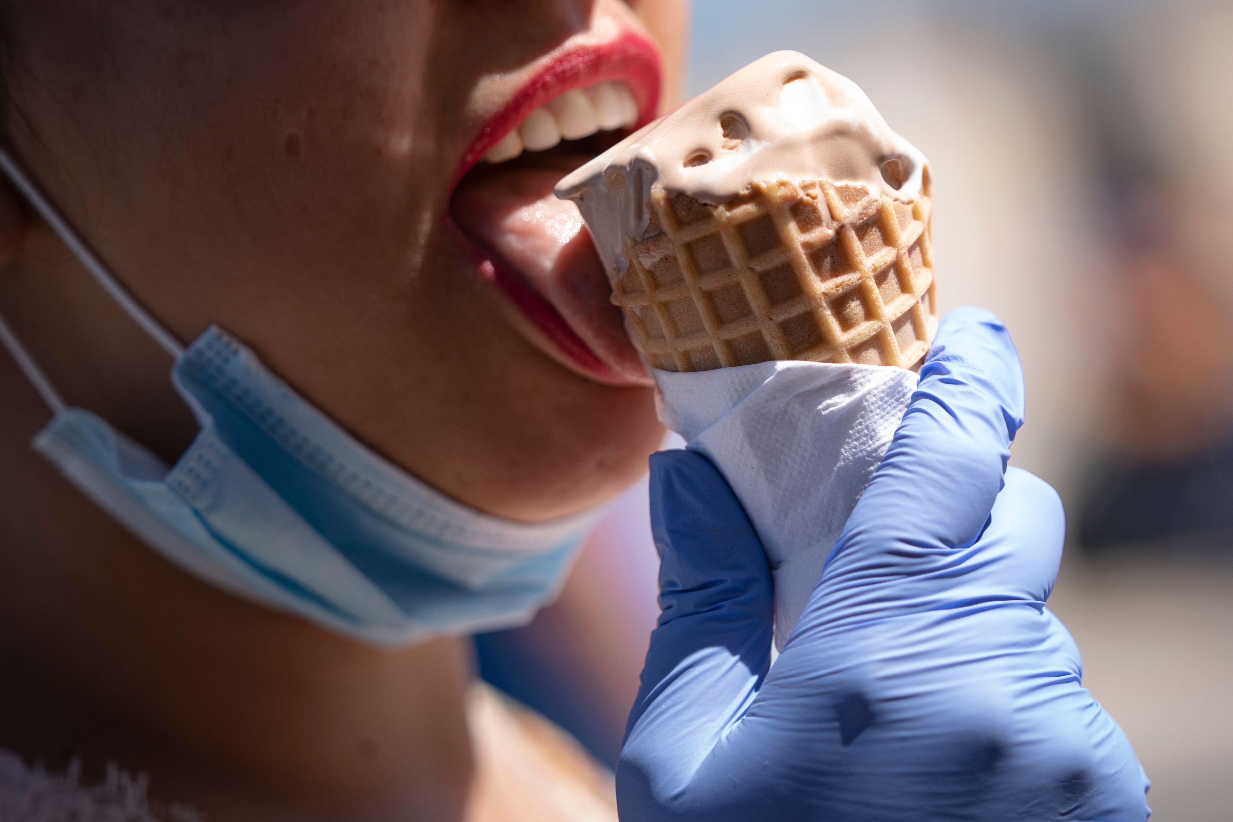 A woman wears gloves as she eats an ice cream cone.