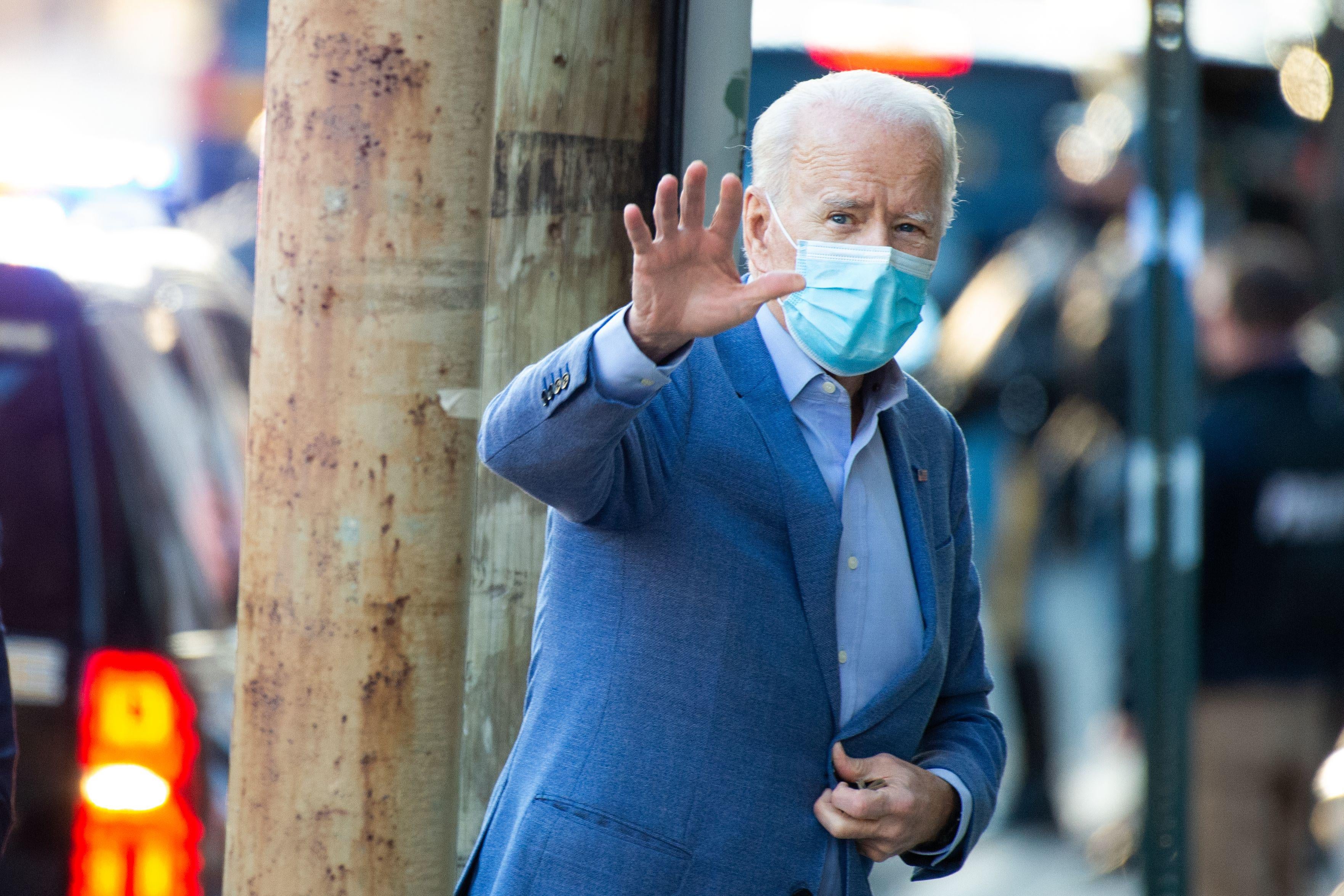 Joe Biden, wearing a medical mask, waves to the camera as he walks into a venue in Wilmington, Delaware
