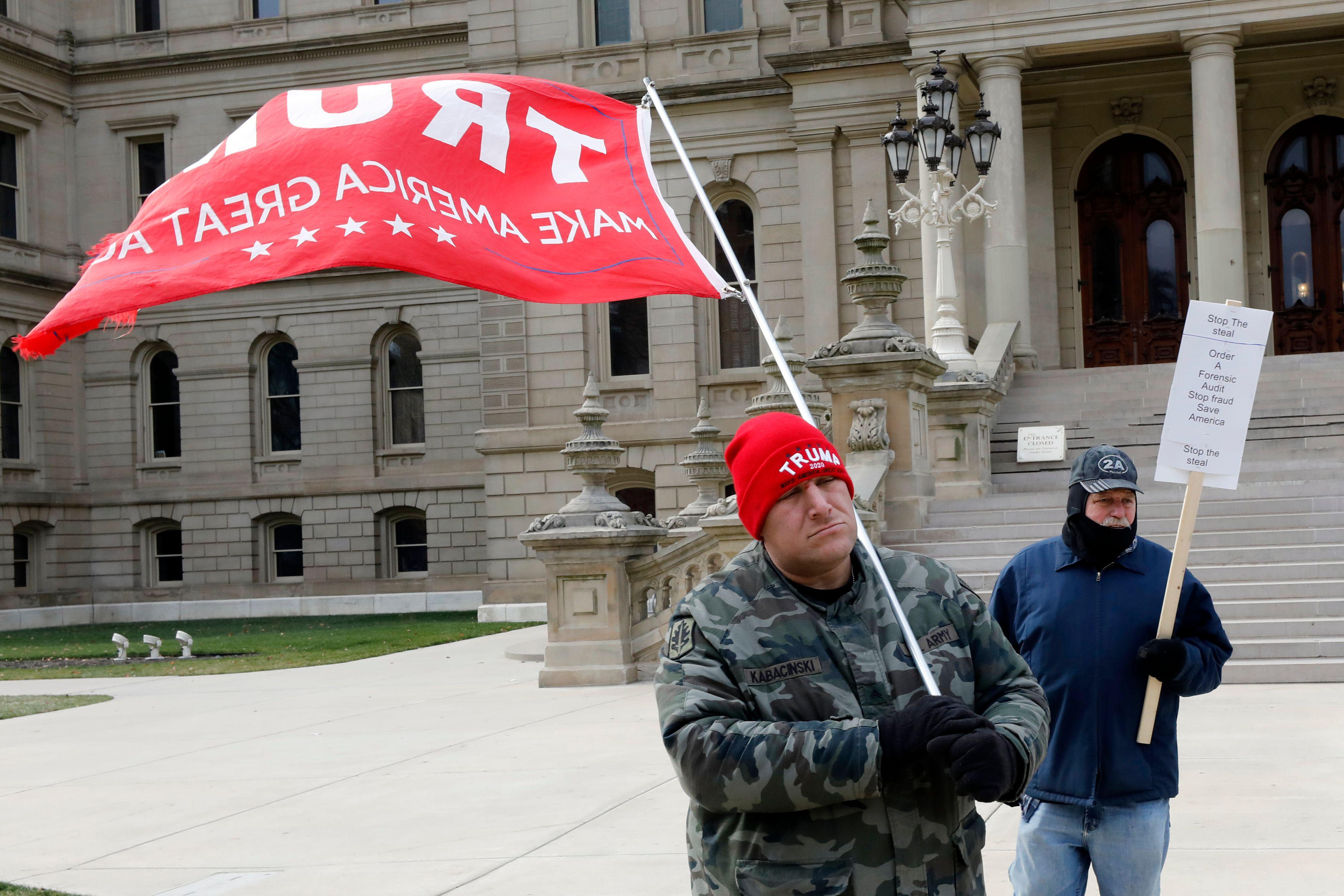 One man in a red Trump beanie carries a large red Trump flag and another man holds a Stop the Steal sign in front of the Capitol steps