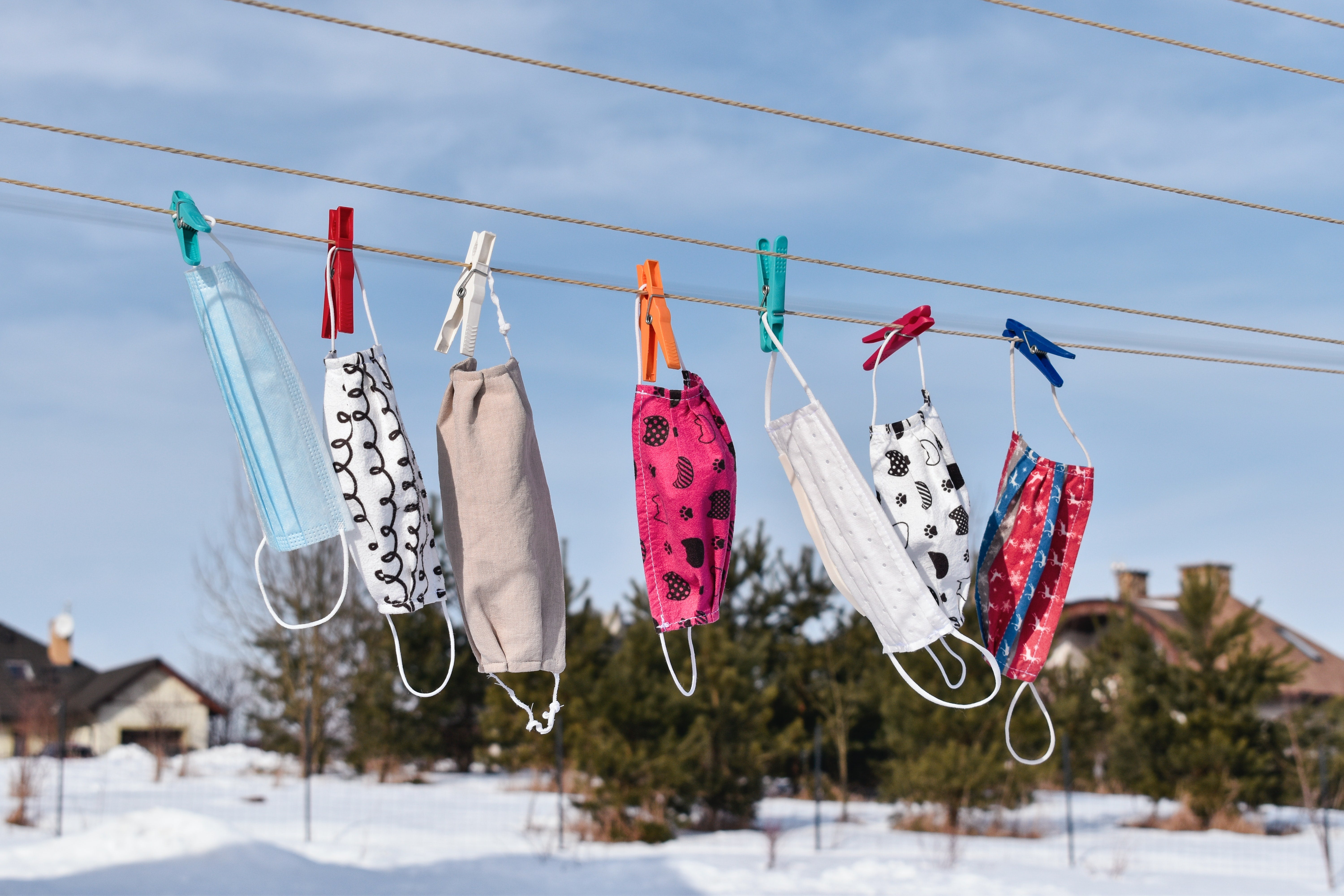 Masks in various colors and designs hanging on a clothesline outside in a snowy area