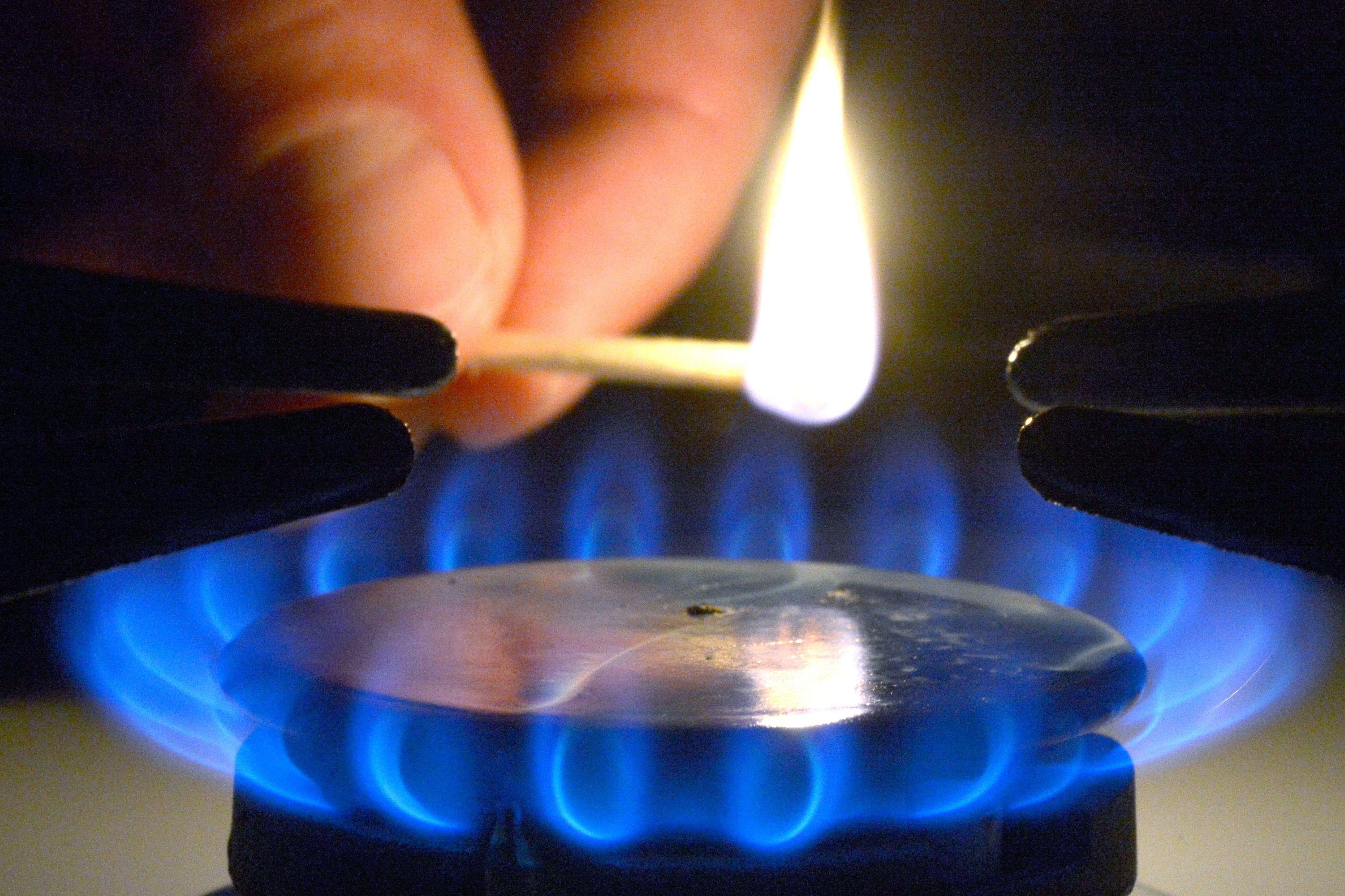 A hand is seen lighting a gas stove with a lit match.