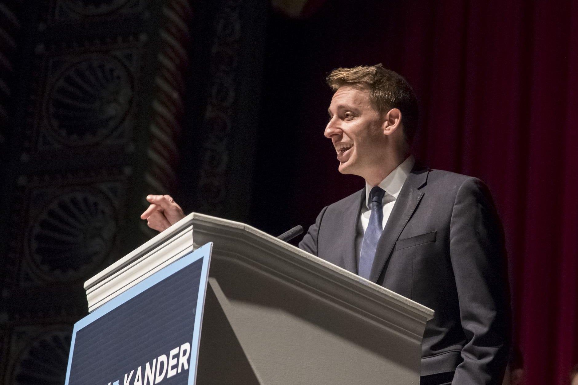 Jason Kander points as he stands behind a podium.
