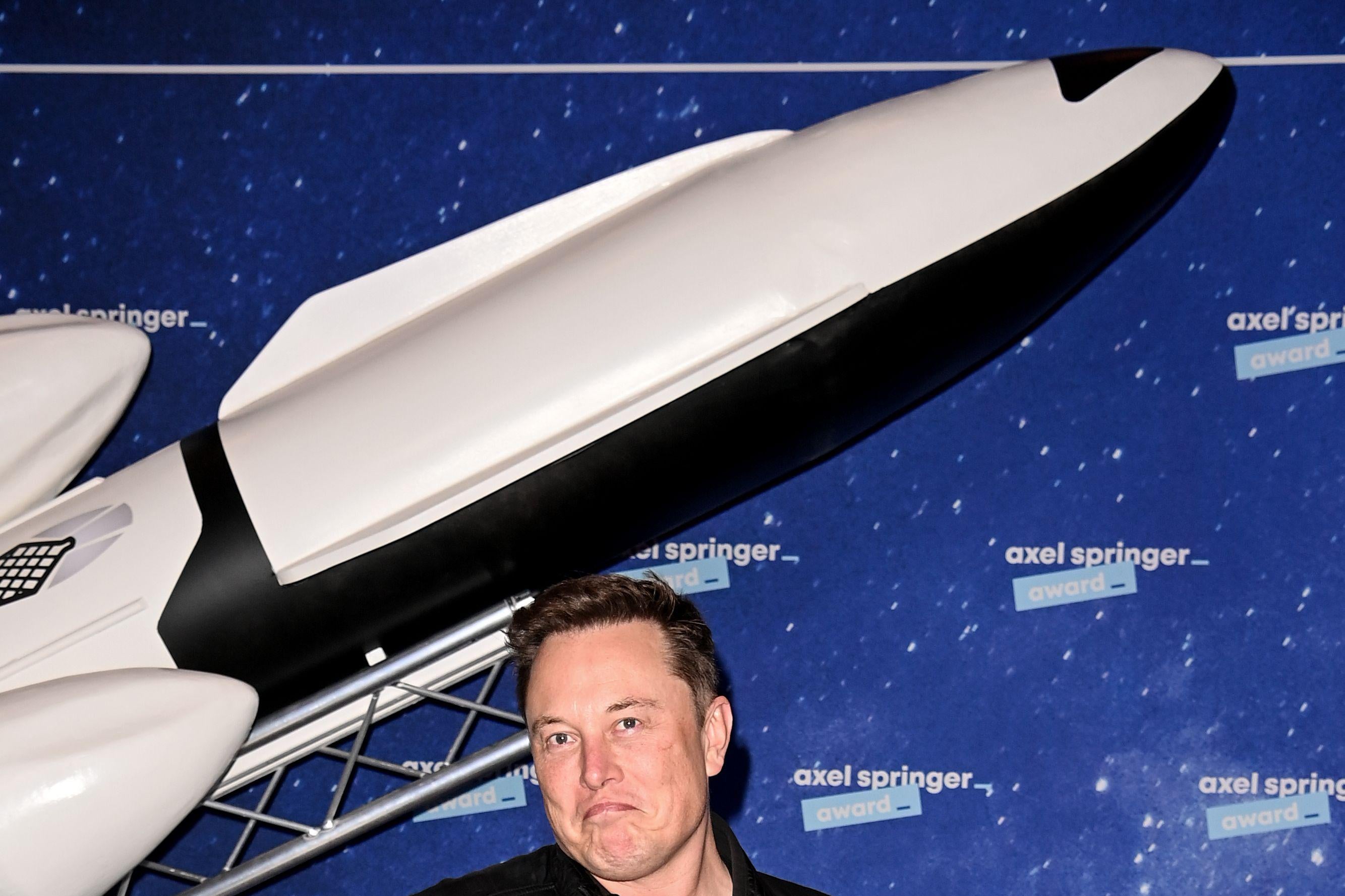 Elon Musk on a red carpet, shrugging.