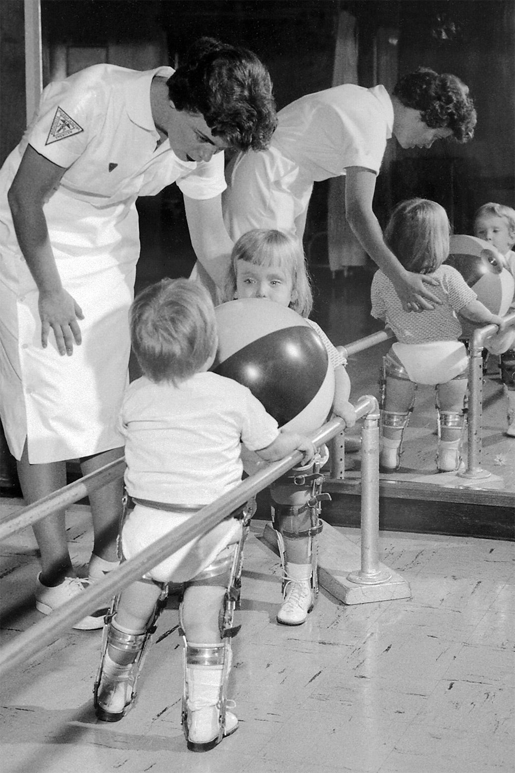 Two small children do physical therapy exercises in leg braces.