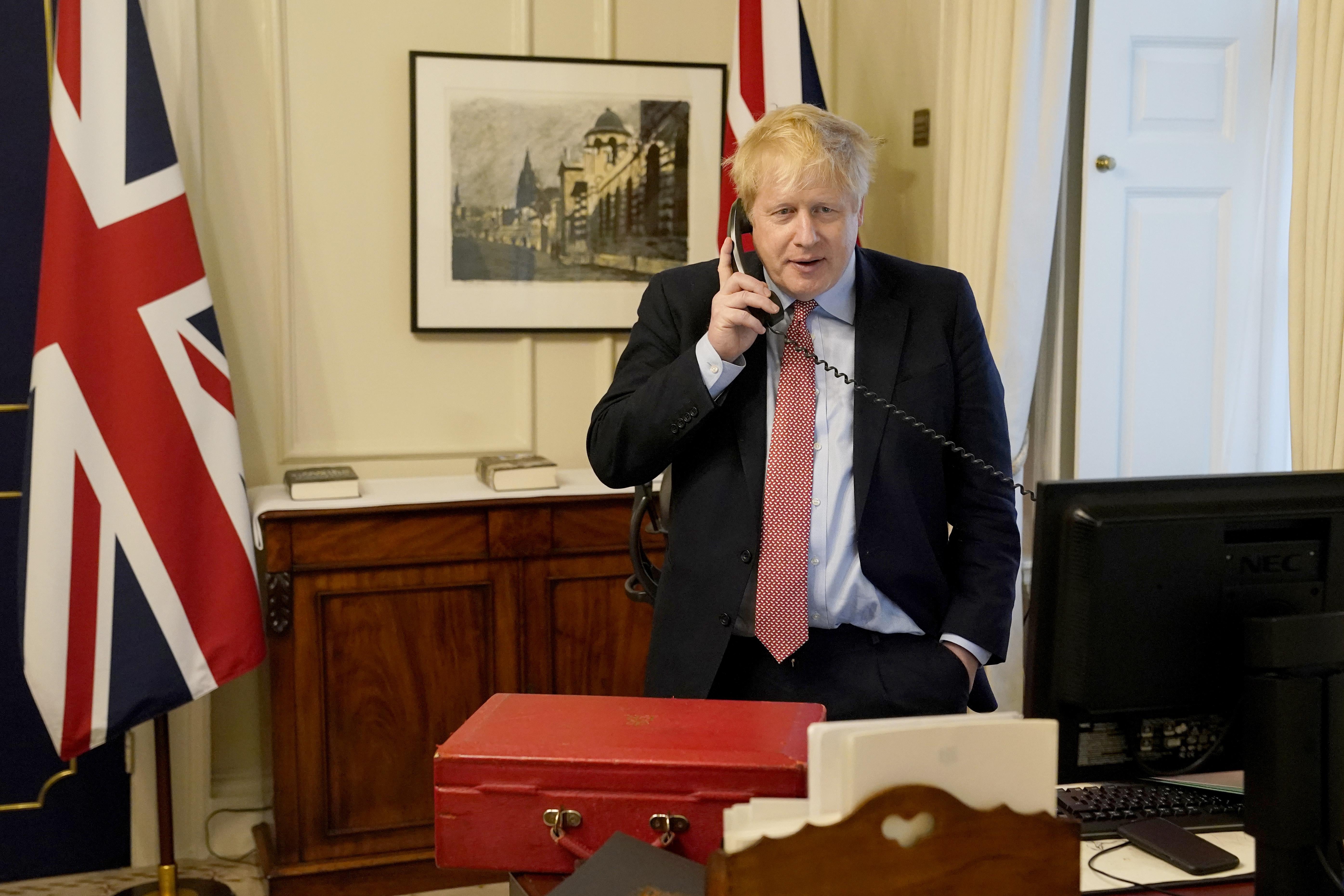 Boris Johnson stands in an office, talking on a telephone.