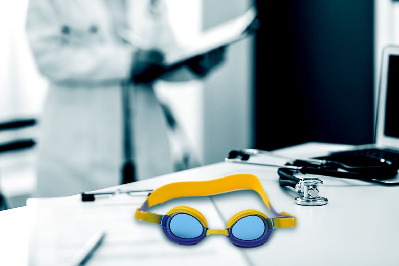 A pair of goggles is seen on a table, on top of papers and next to a stethoscope. In the background, a doctor can be seen looking at a clipboard.