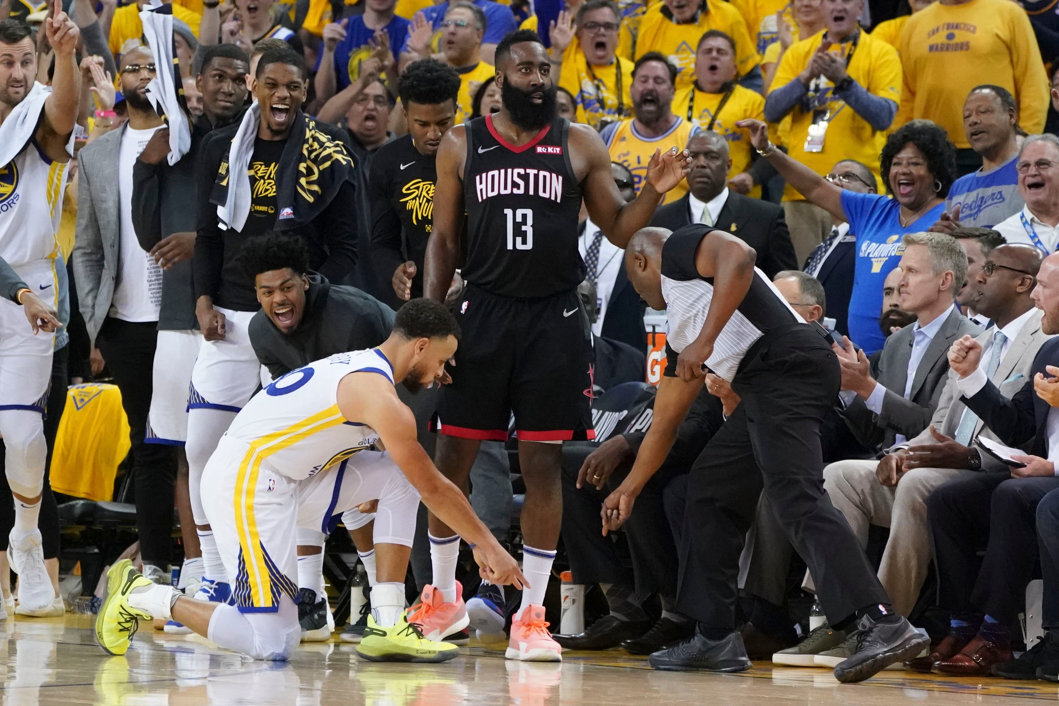 Curry, kneeling, points at the sideline as Harden looks past him with a stoic expression.