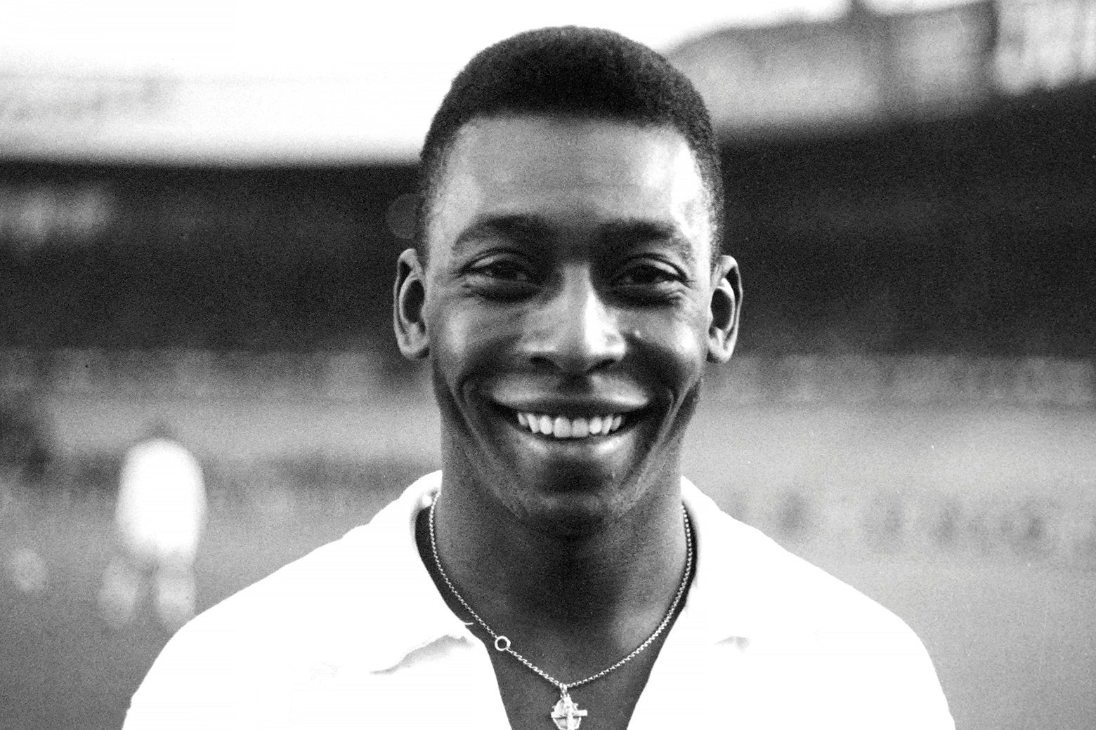 Pelé on the pitch smiling at the camera in a jersey and a necklace.