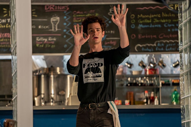 Andrew Garfield dressed as a diner waiter holds his hands up with his eyes wide and mouth open.