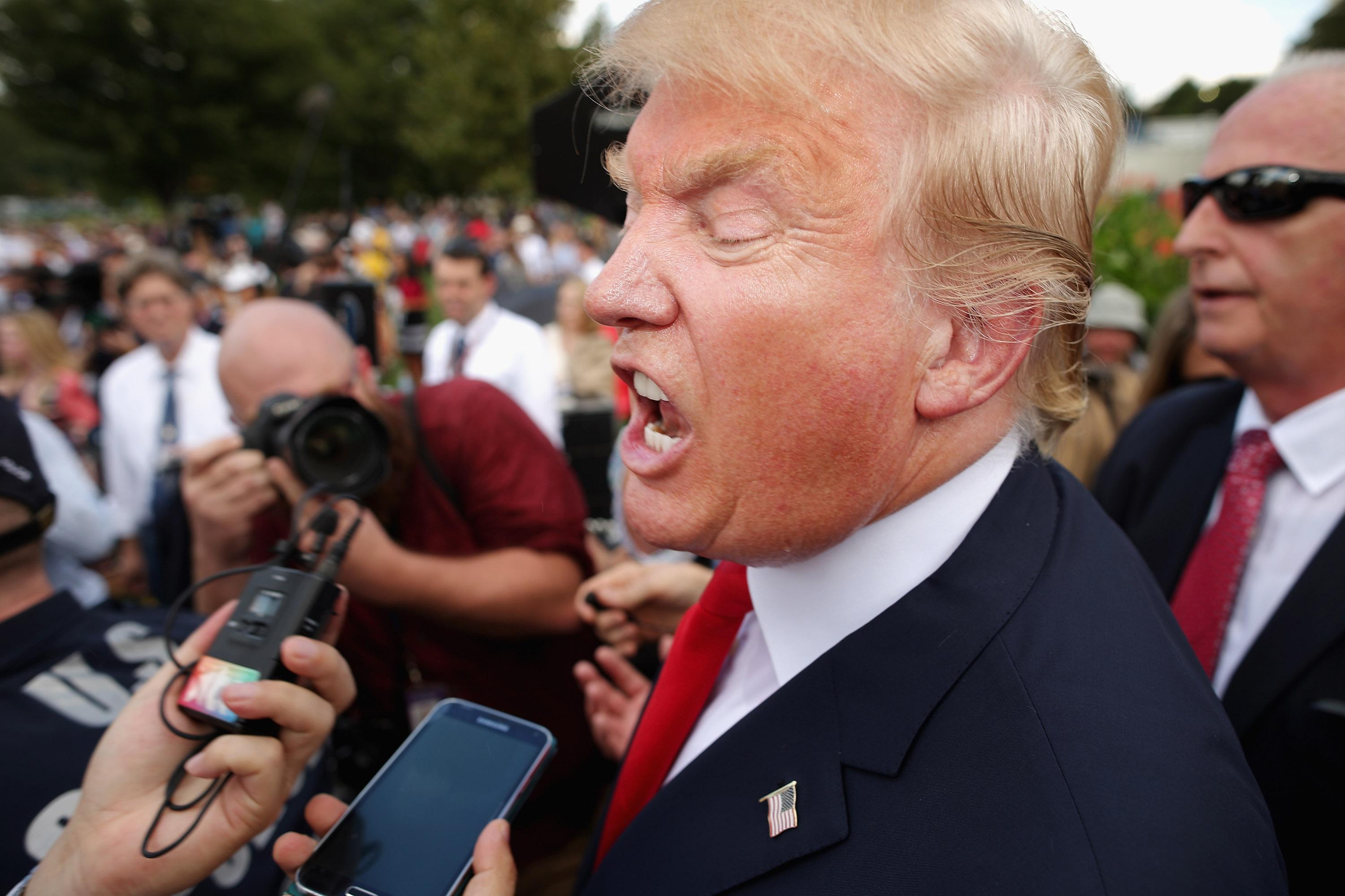 Donald Trump, surrounded by a crowd of people, yells into a voice recorder.