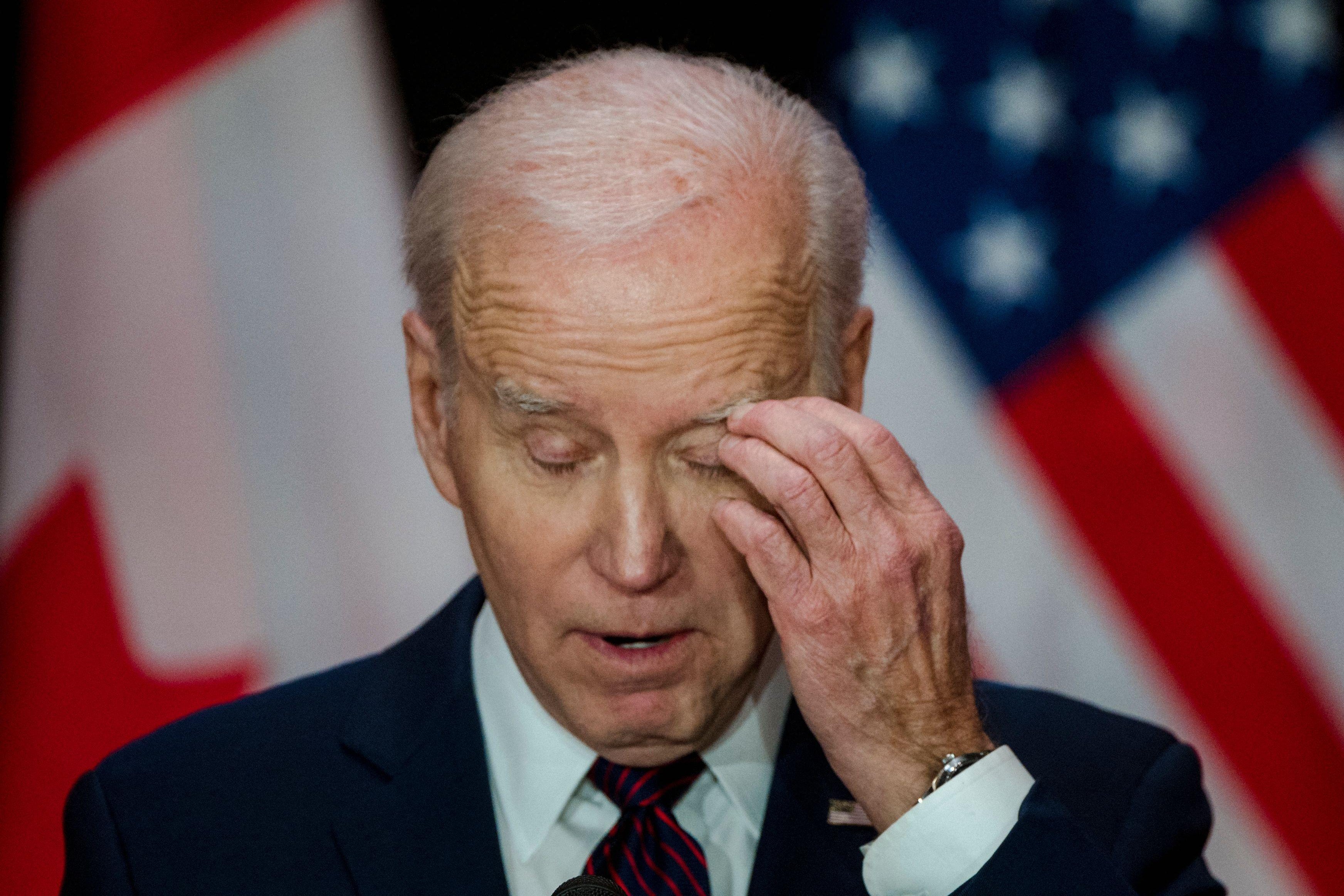 Biden looks down and scratches his left eye with his left hand