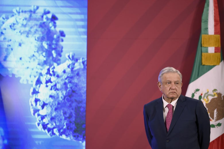 Andrés Manuel López Obrador stands in front of a Mexican flag and a projected image of the novel coronavirus.