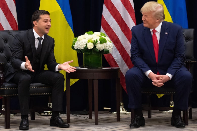 Zelensky smiles and gestures beside Trump smiling at him, both men seated with Ukrainian and U.S. flags behind them.