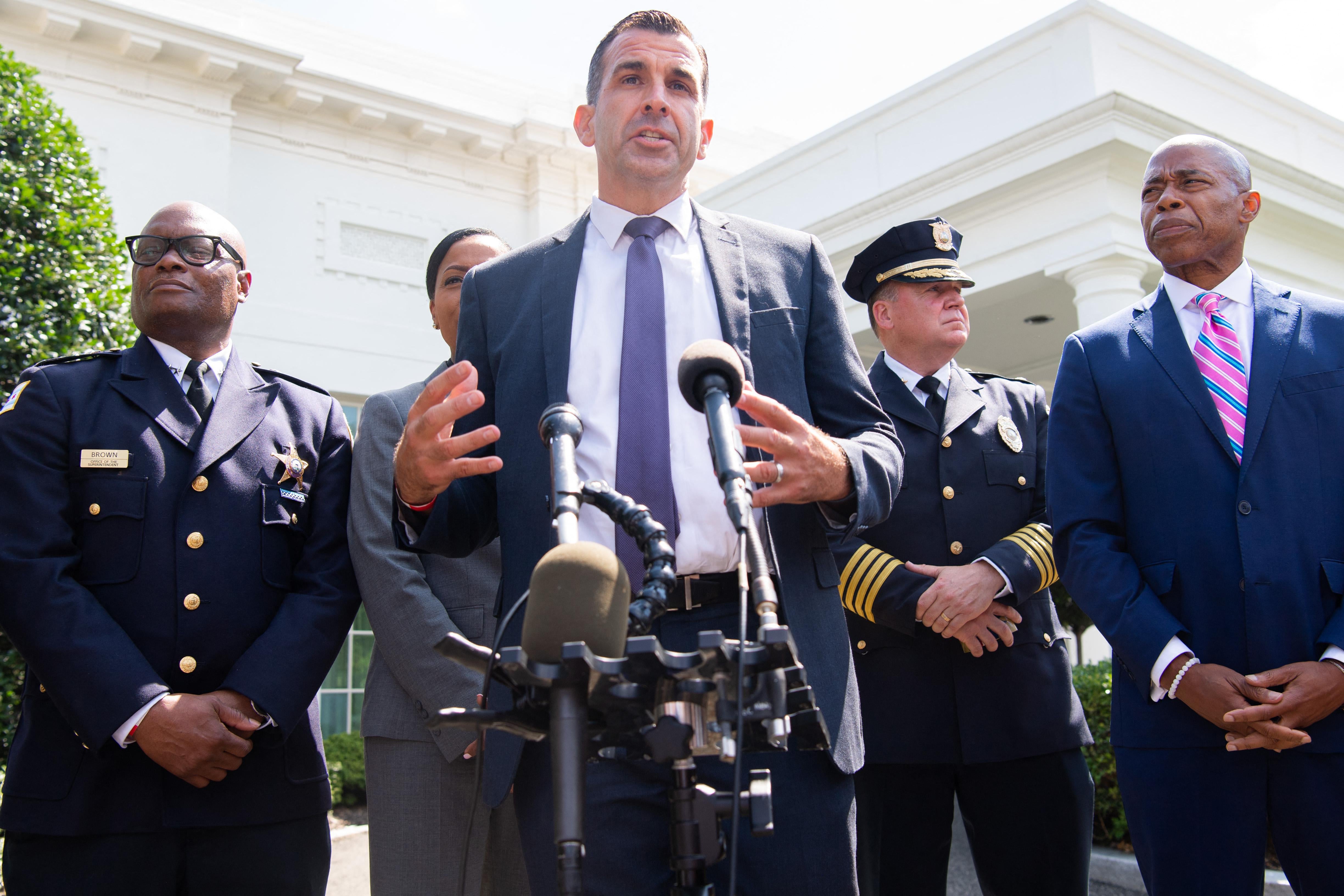 Liccardo stands speaking at a mic with Adams and law enforcement officials around him outside the West Wing of the White House