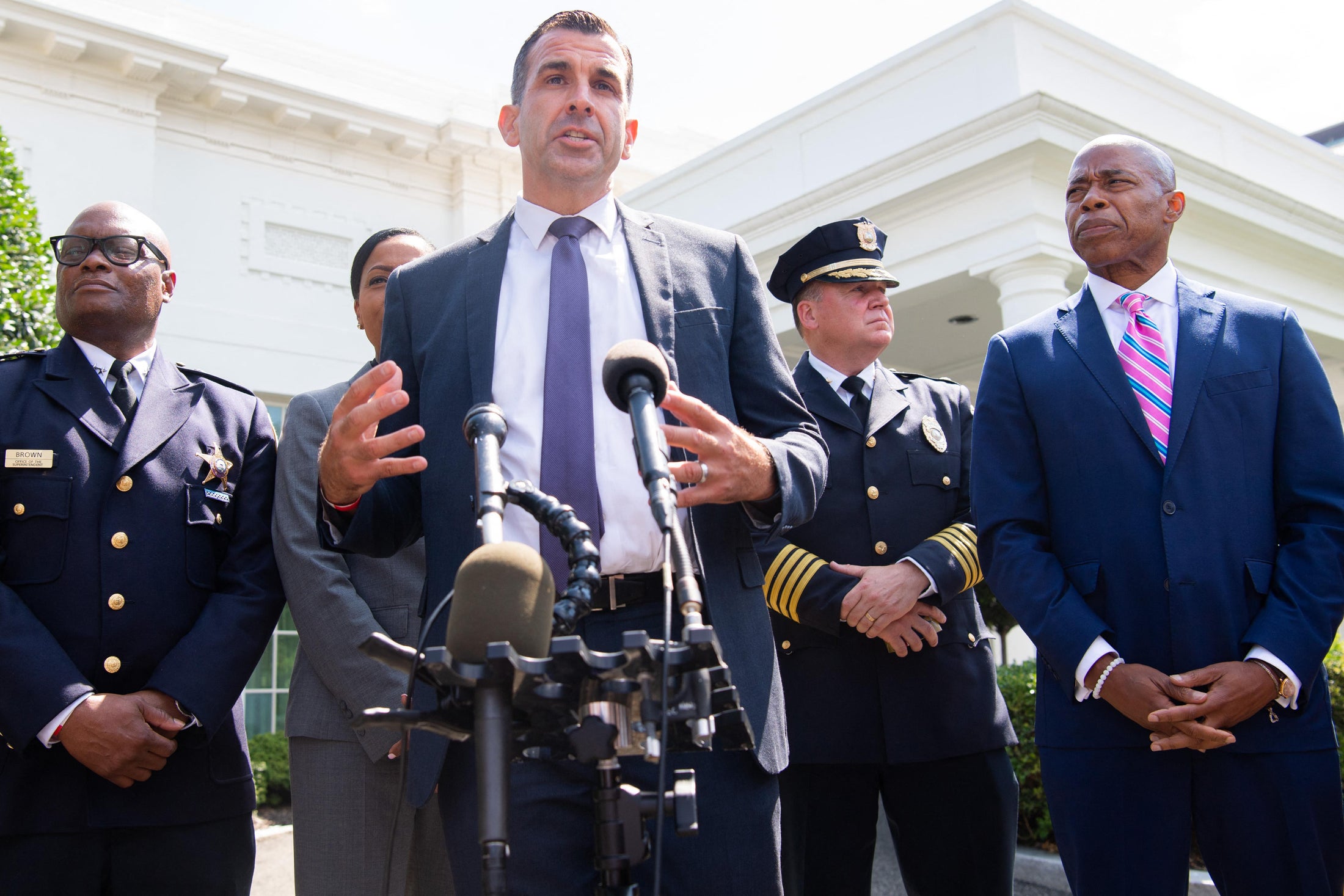 Liccardo stands speaking at a mic with Adams and law enforcement officials around him outside the West Wing of the White House